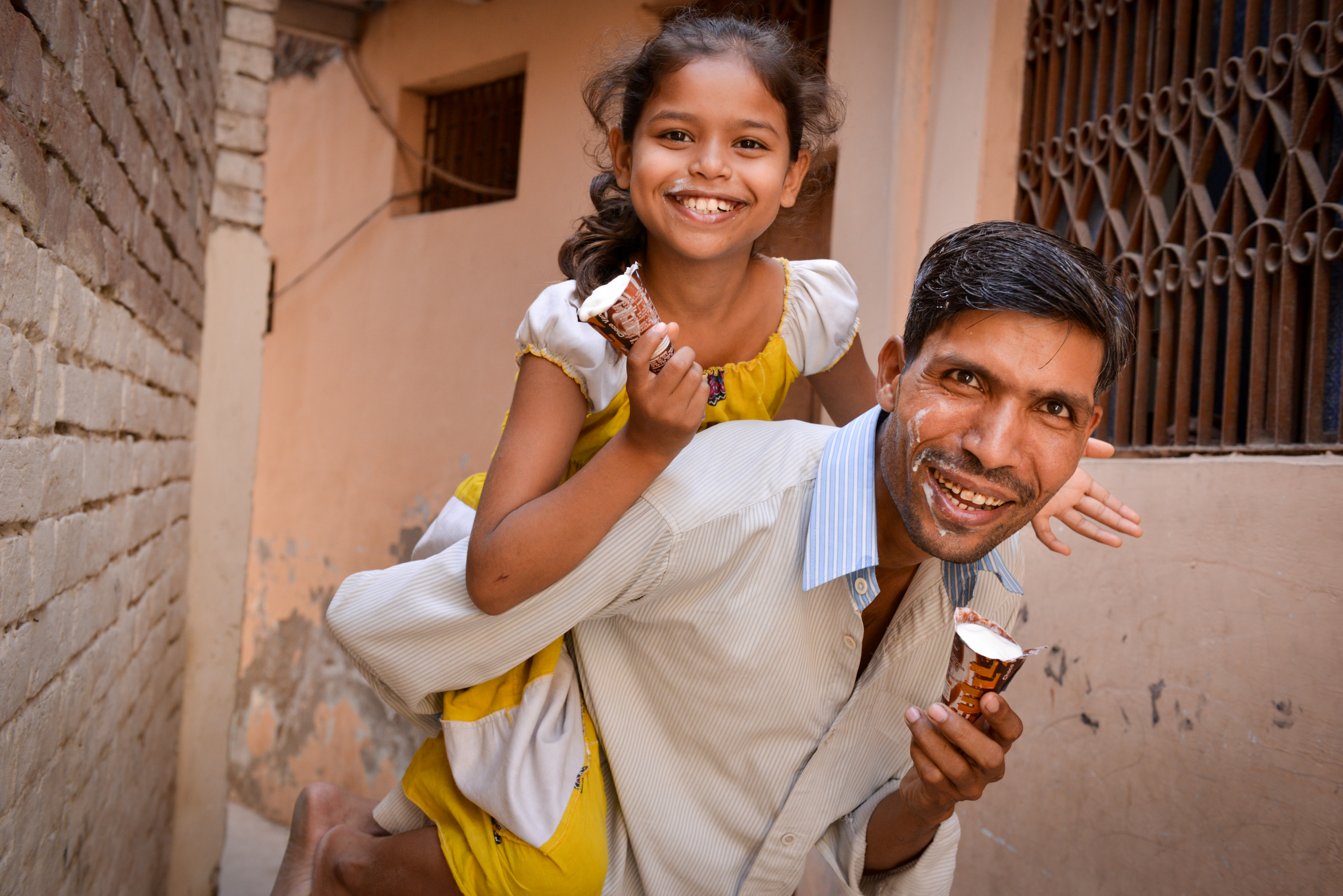 Mangay and his daughter smile as they eat ice cream and he gives her a piggy back 