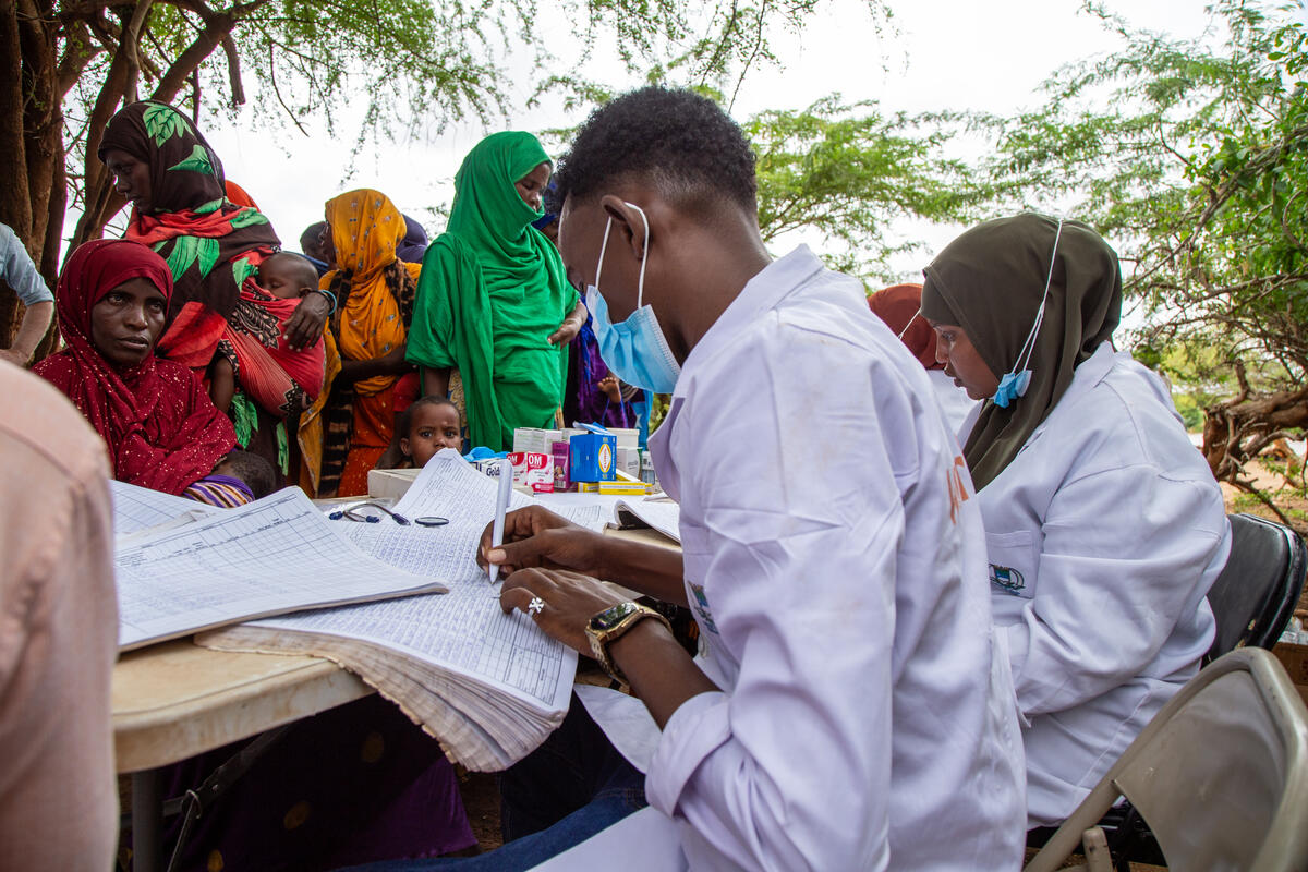 World Vision staff sat at table to distribute cash to queue of Somali parents