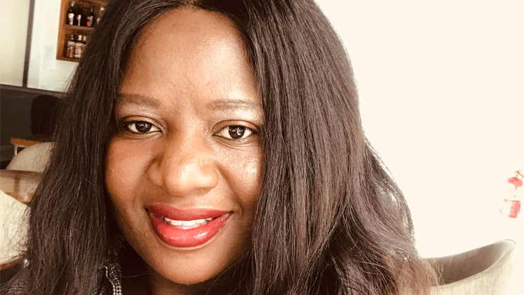 UK woman smiles at the camera, in a house with photo behind
