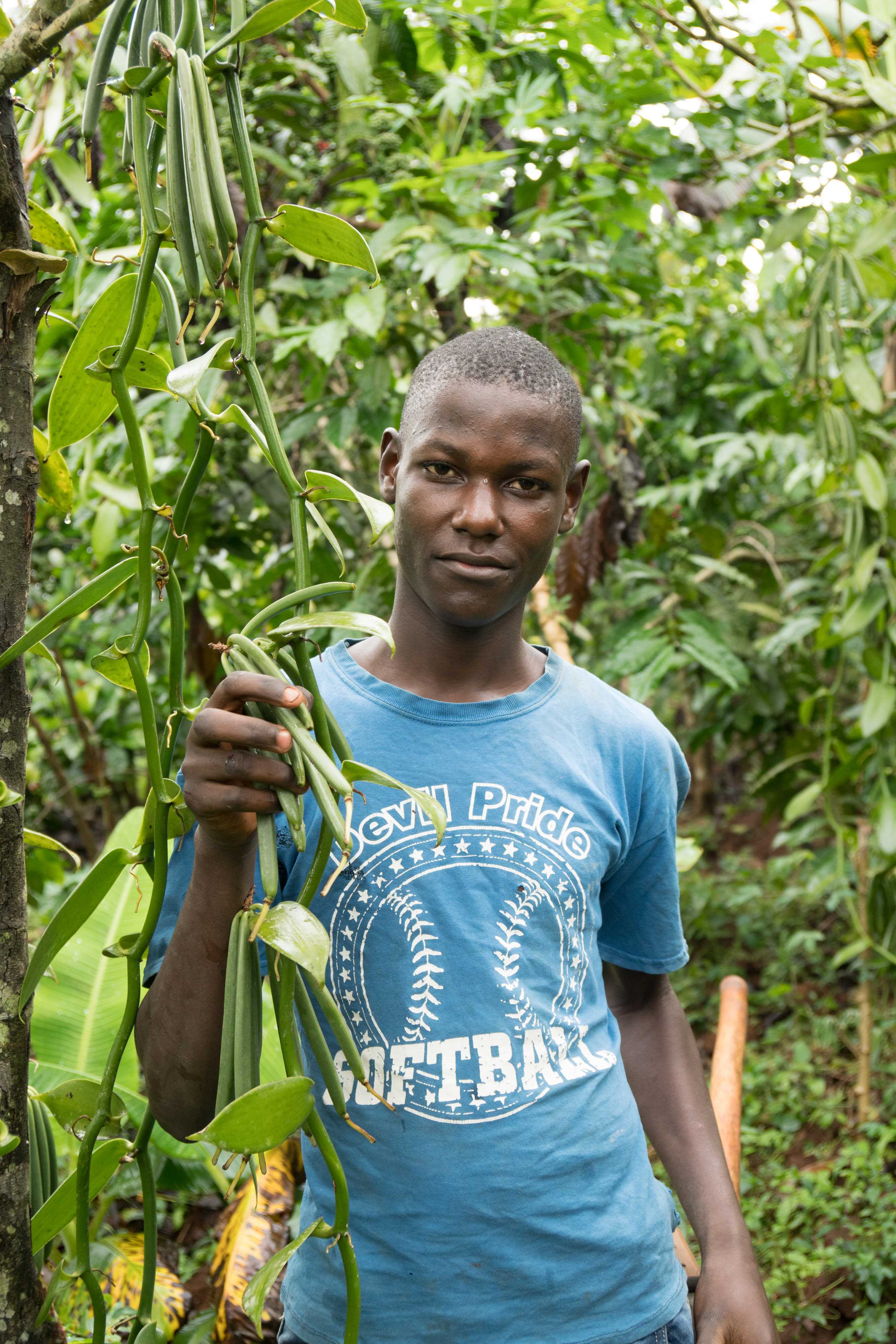 Girl sits on the floor next to the embers she sells to support her family in DRC, as a person walks past