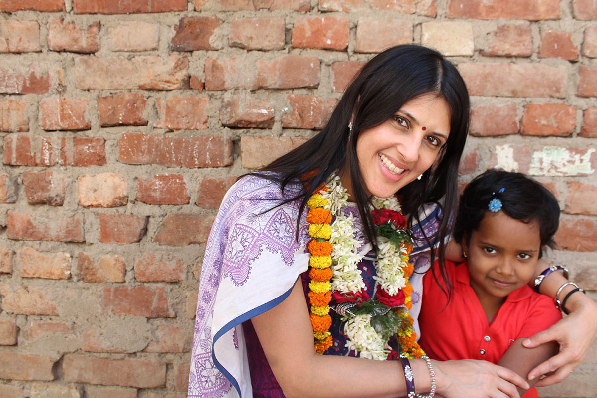 Sponsored girl in India sits cradled by her sponsor, both smiling at the camera