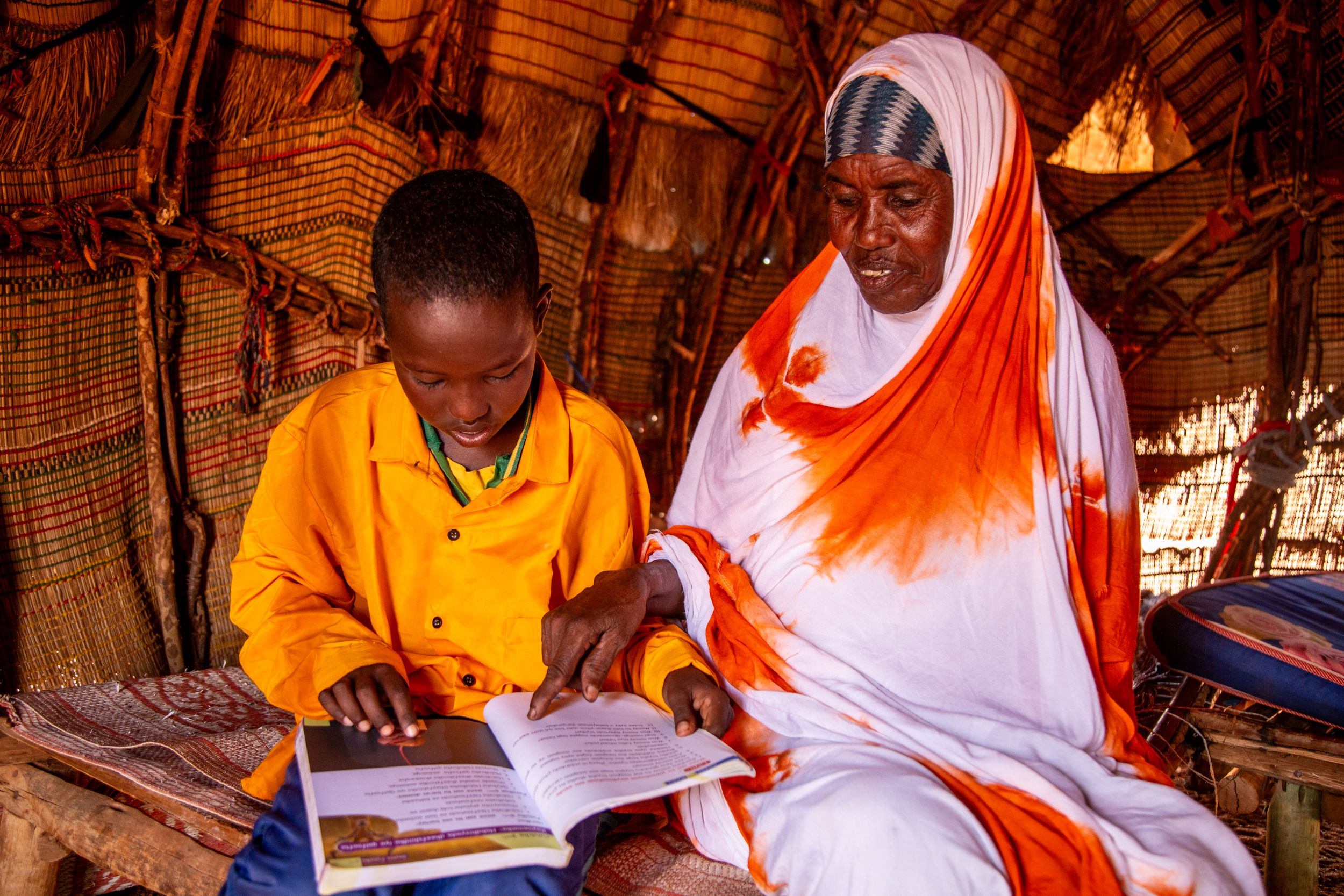 Boy and his grandmother sitting inside their home, looking at an open school book together