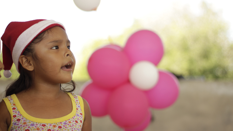 Girl in the UK wears a Christmas hat and sits in front of pink and white balloons