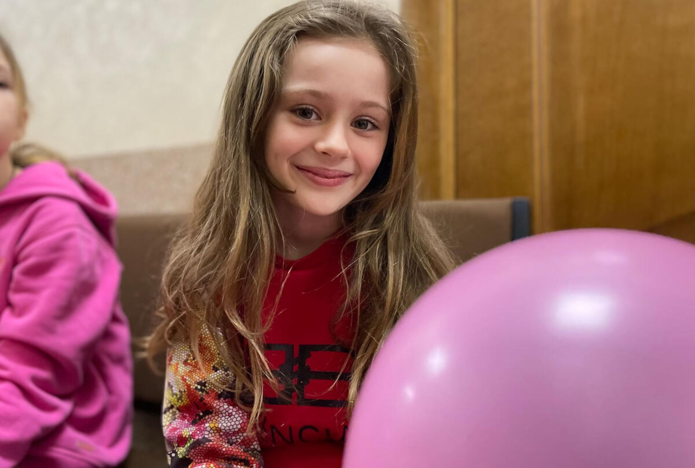 A young Ukrainian girl smiles into the camera while holding a pink balloon
