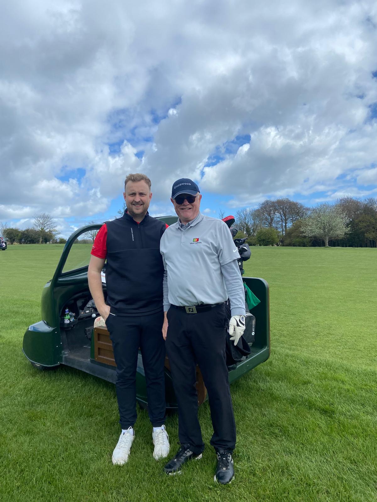Two golfers stand in front of a buggy at a corporate golf day