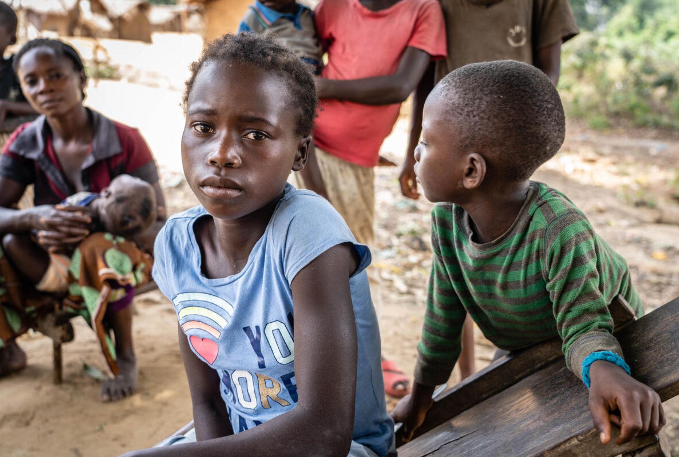 12-year-old girl from DRC looking worriedly at the camera, her family are in the background