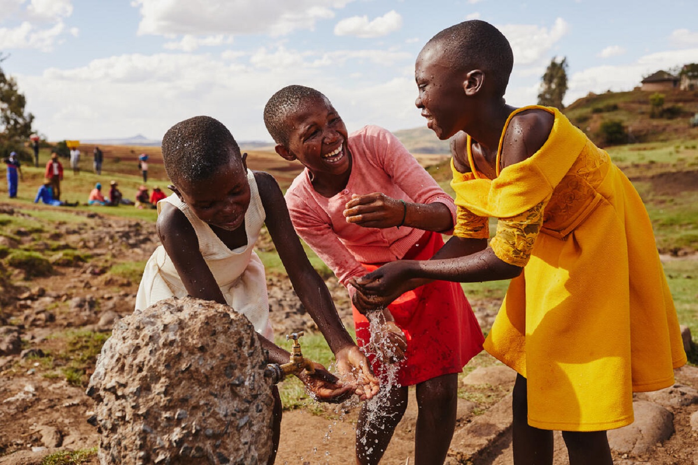 Three children smiling as they get collect clean water