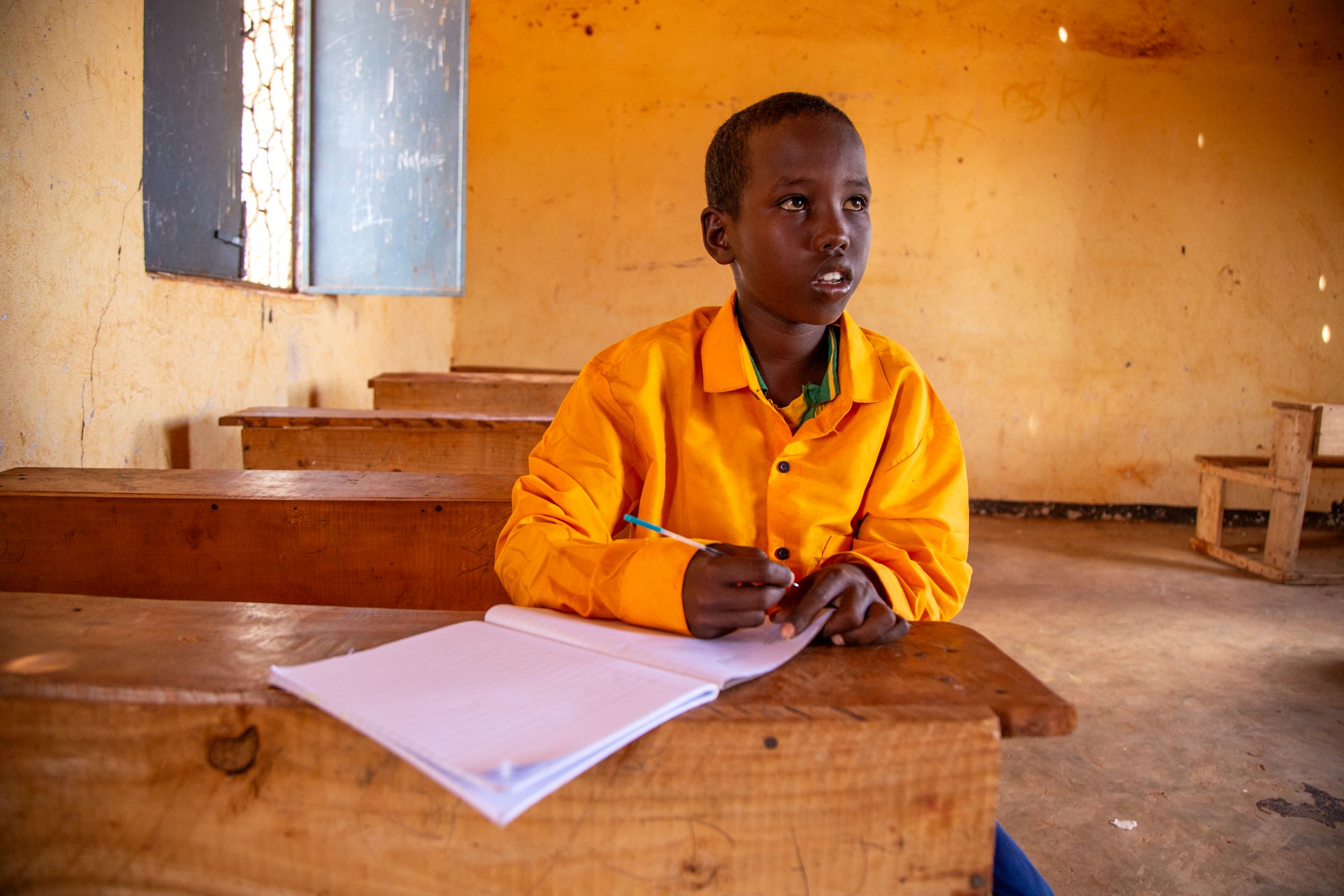 Hungry boy sitting at his school desk in an empty classroom