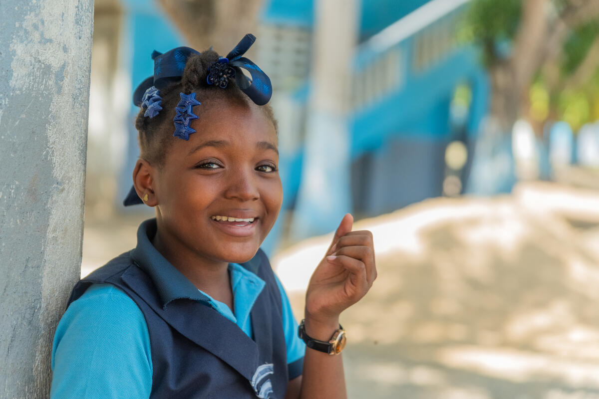 A sponsored child in Haiti smiles at the camera leaning her back on a wall