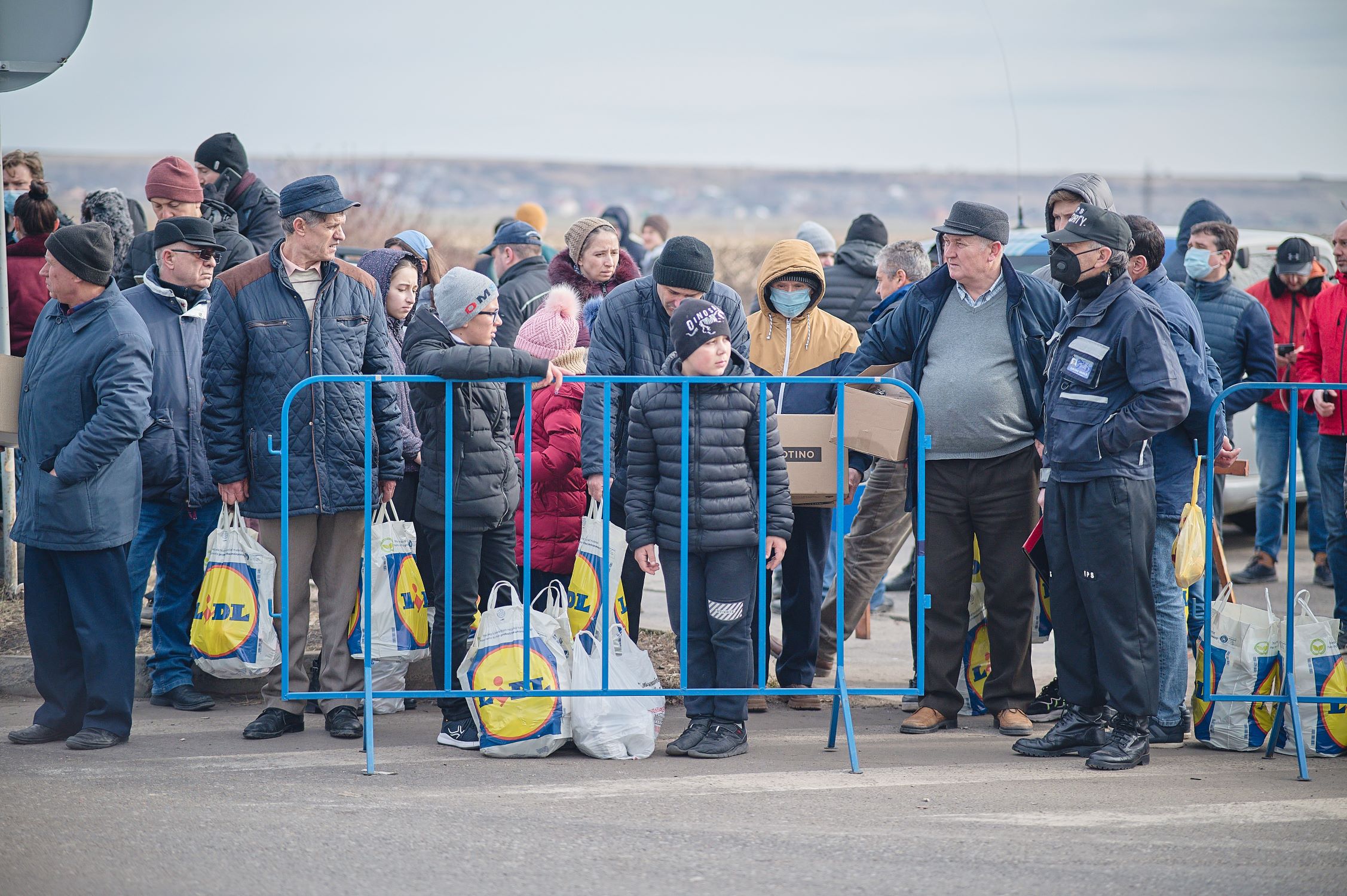 Ukrainian people stand behind a barrier with their belongings