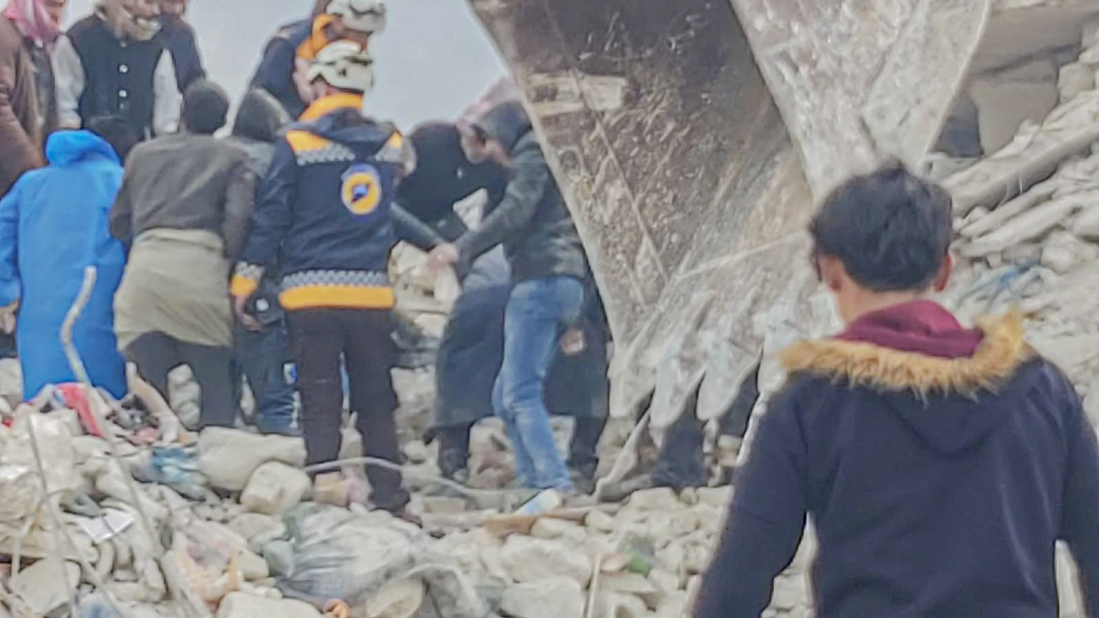 Syrian boy walking towards a group of rescuers digging in rubble after the earthquake.