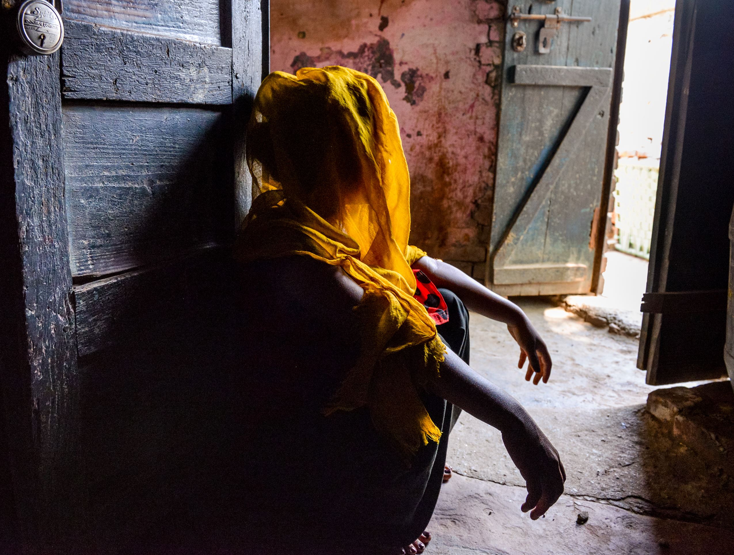A girl looks out of her door in India, face hidden as she recounts her 