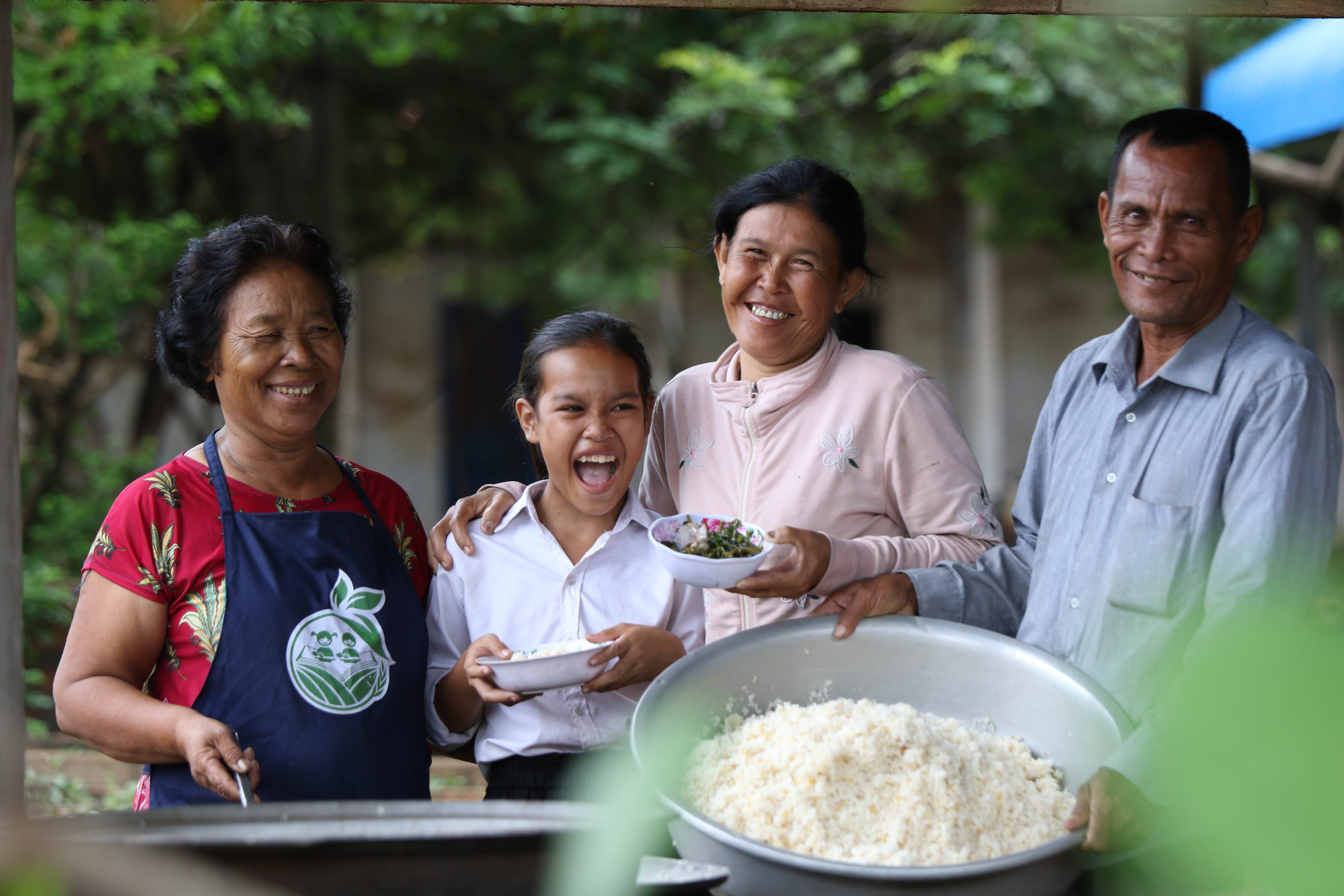 A family of four from Cambodia smiling at the camera with a large bowl of rice