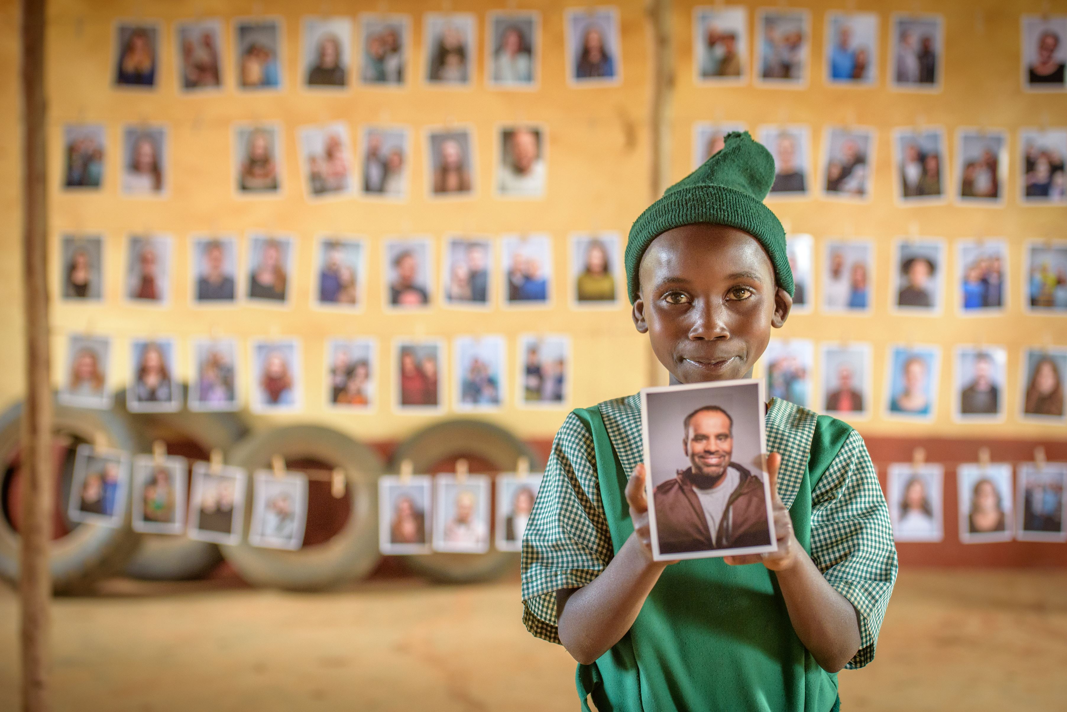 Girl in Uganda in a green dress holds a photo of the person she has chosen as her sponsor