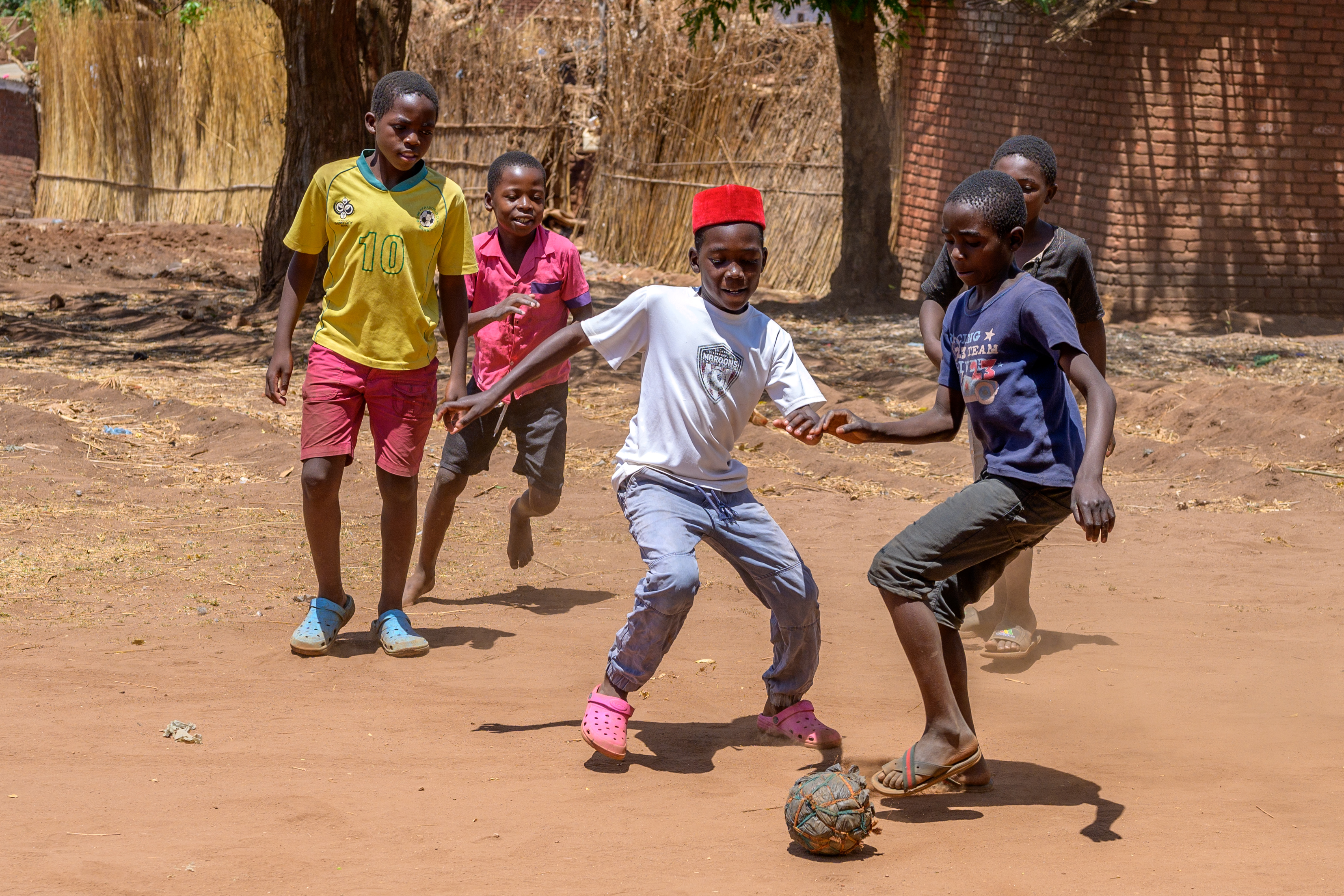 Four young boys play football together, outside in the sun
