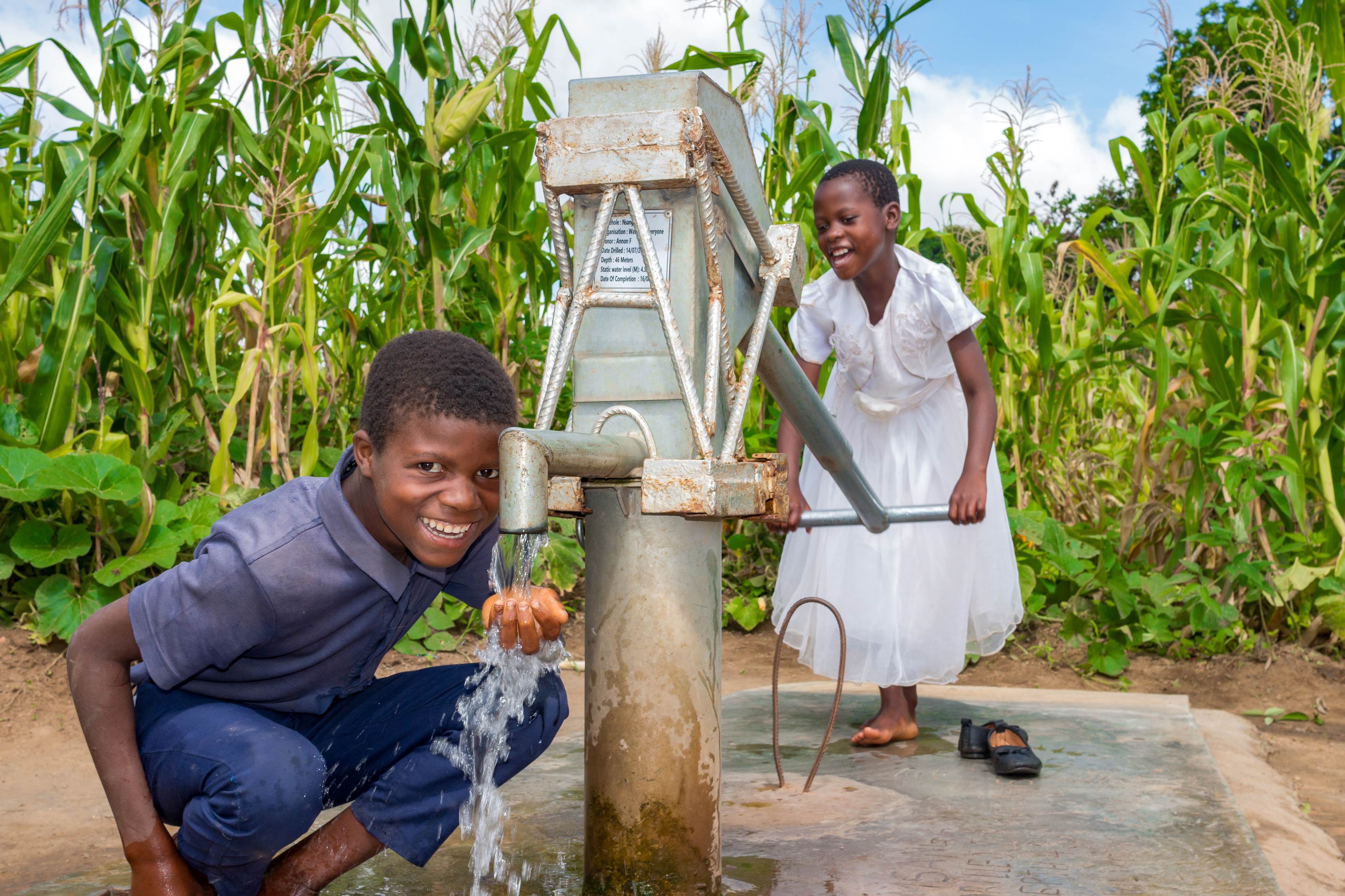 Two children pumping water from a well
