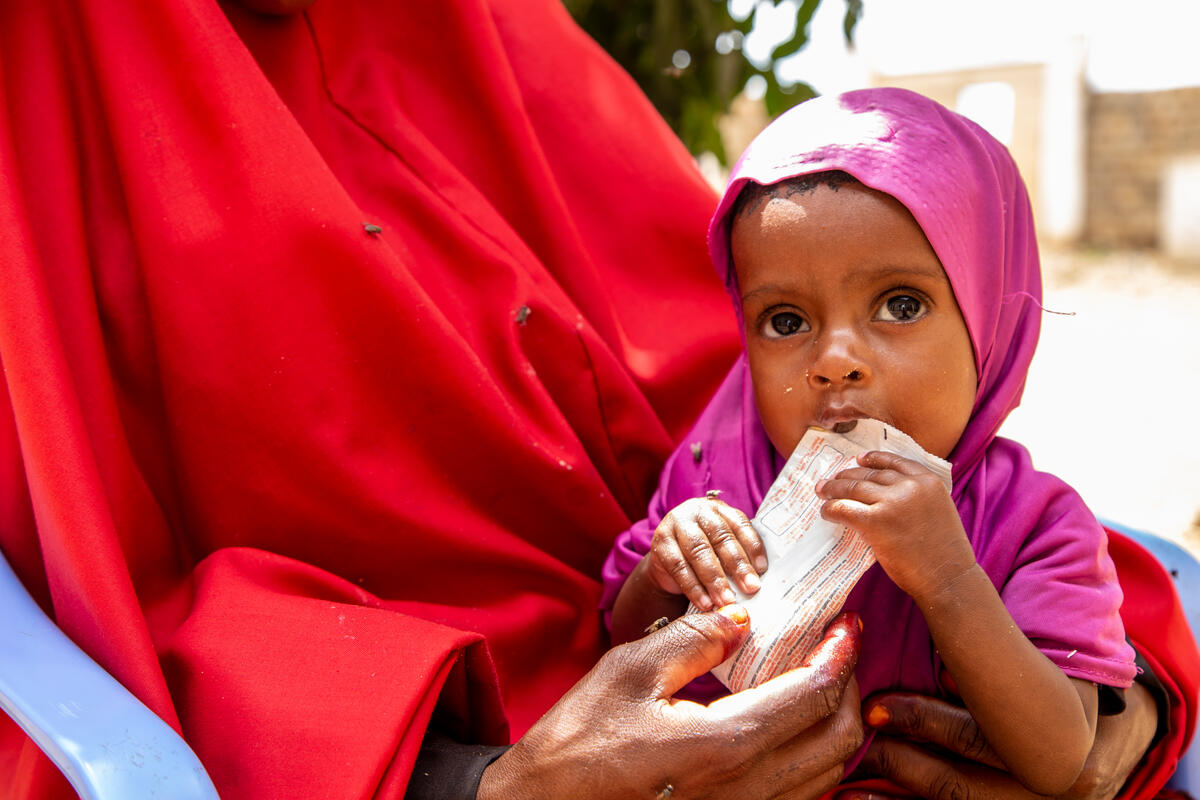 A young girl eats on her mother's lap