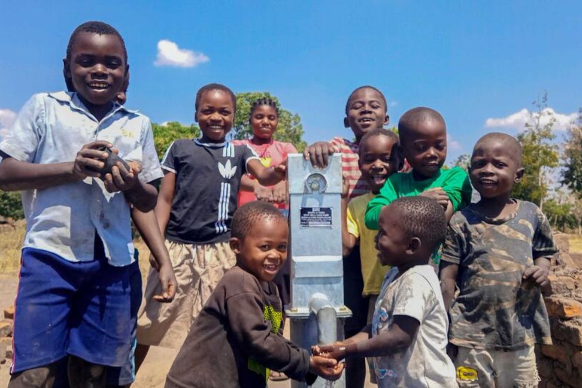 Children in Malawi smile, and huddle around their new clean water tap