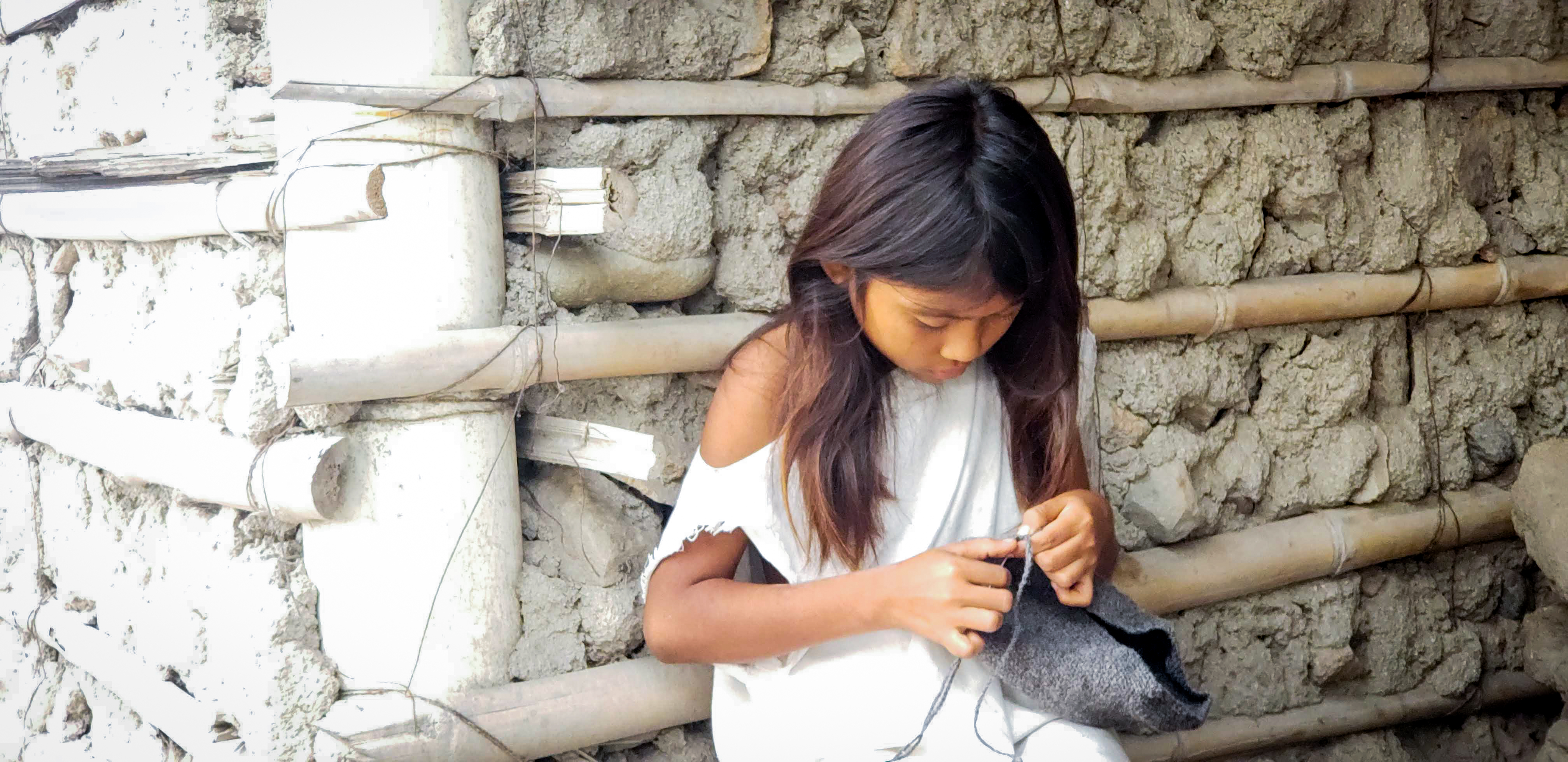 Girl in Columbia sits against a wall as she weaves bags during COVID-19