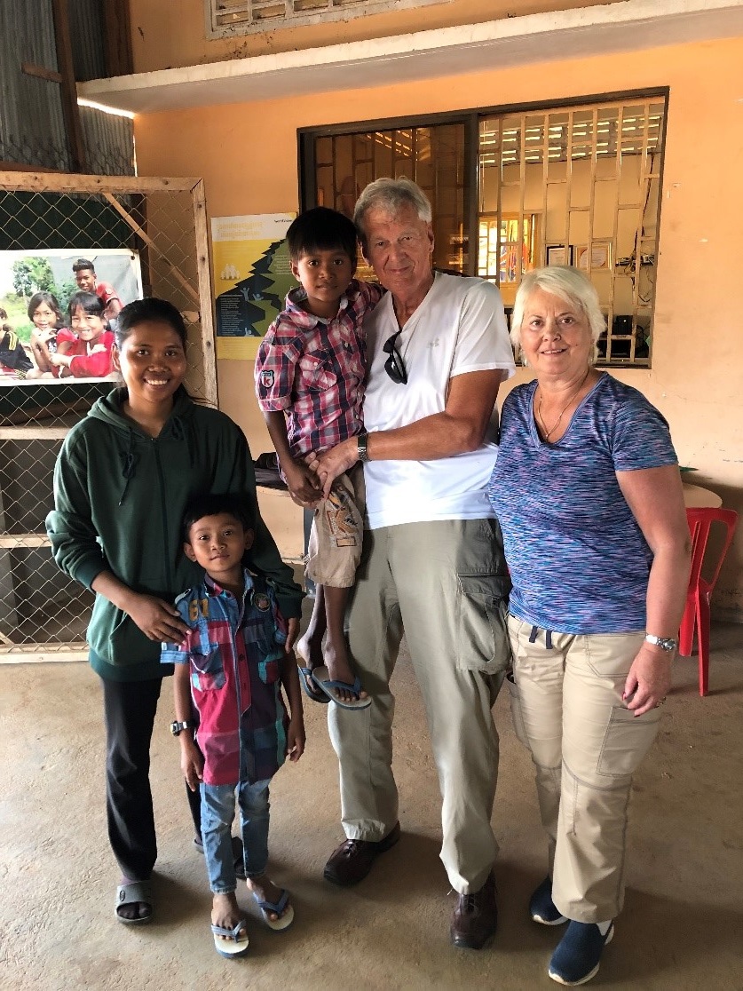 Three adults stand, one holding a child, another child standing, in a room in Cambodia