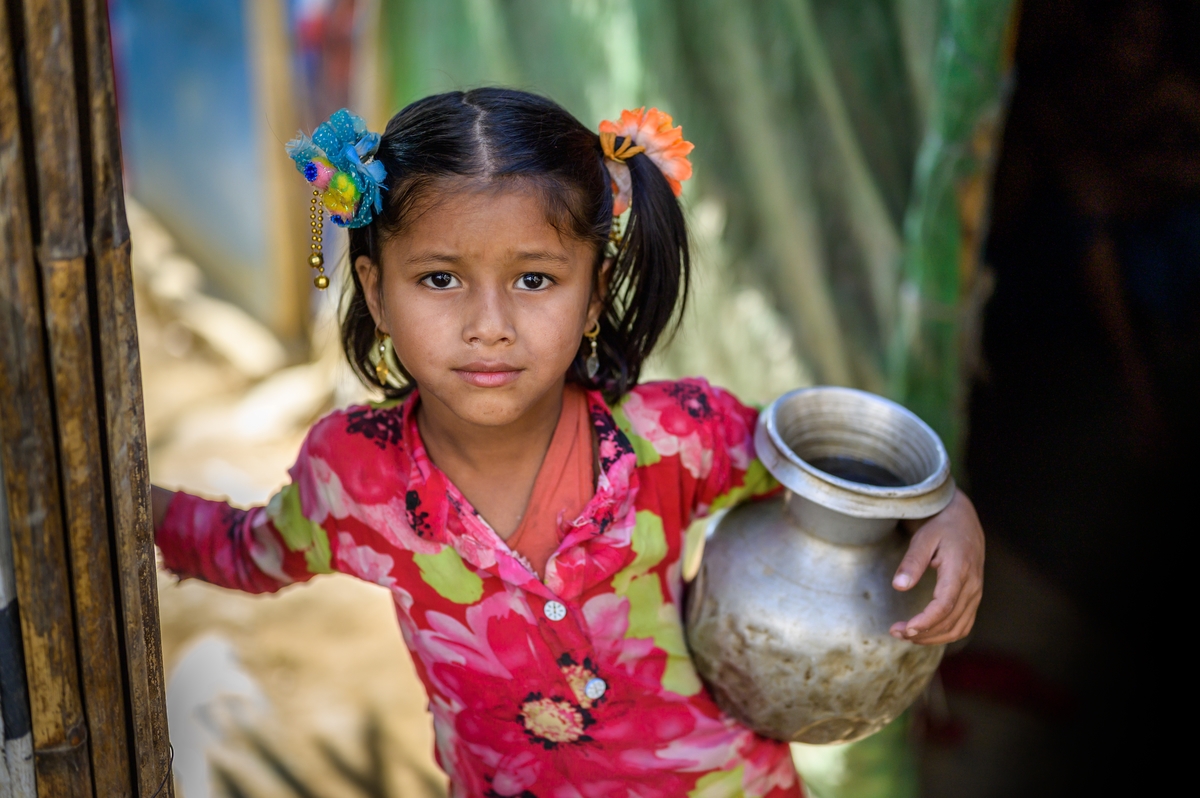 A child in Bangladesh holds a water tankard under her arms as she walks through a doorway