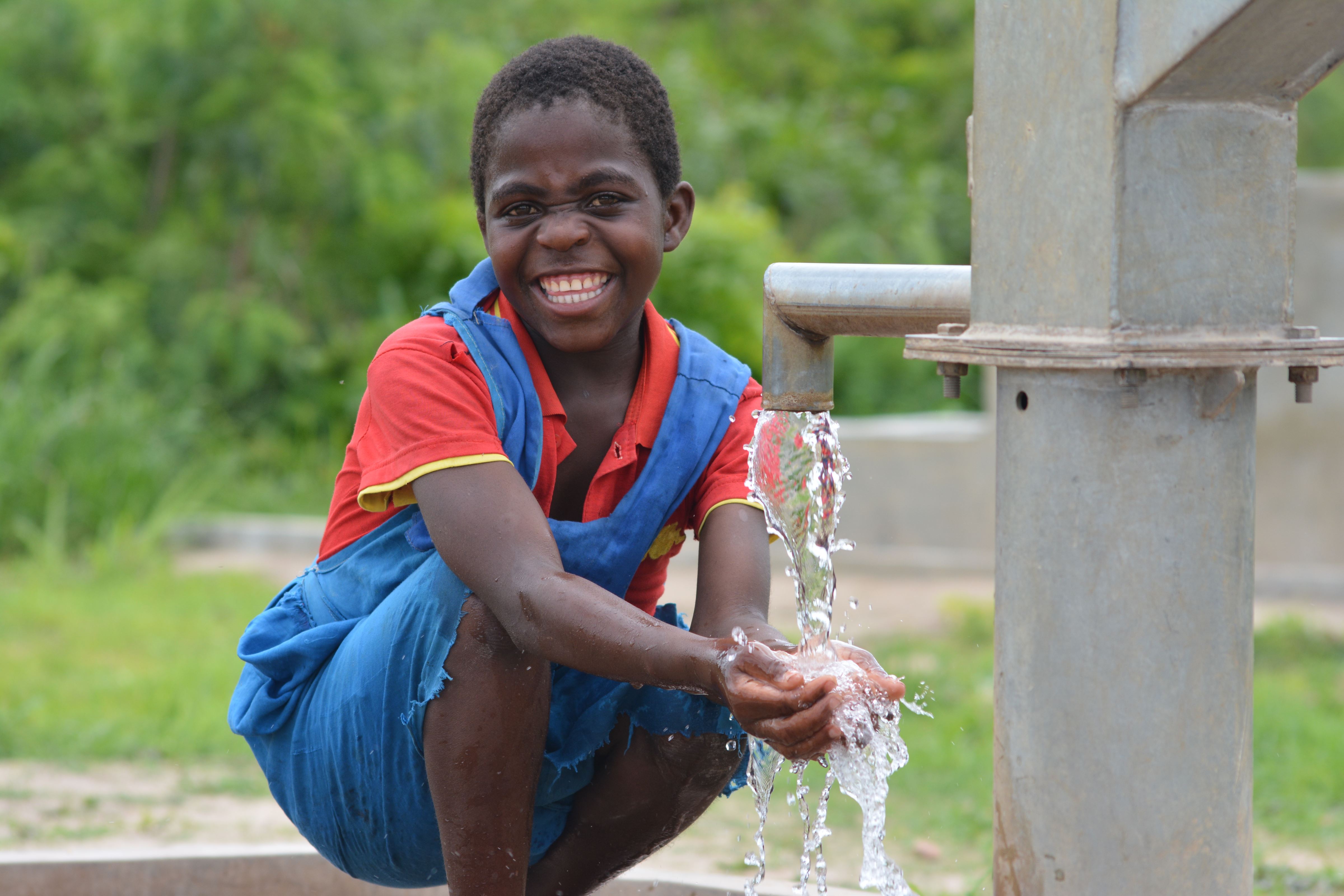 Girl in Malawi smiles as she washes her hands in clean water