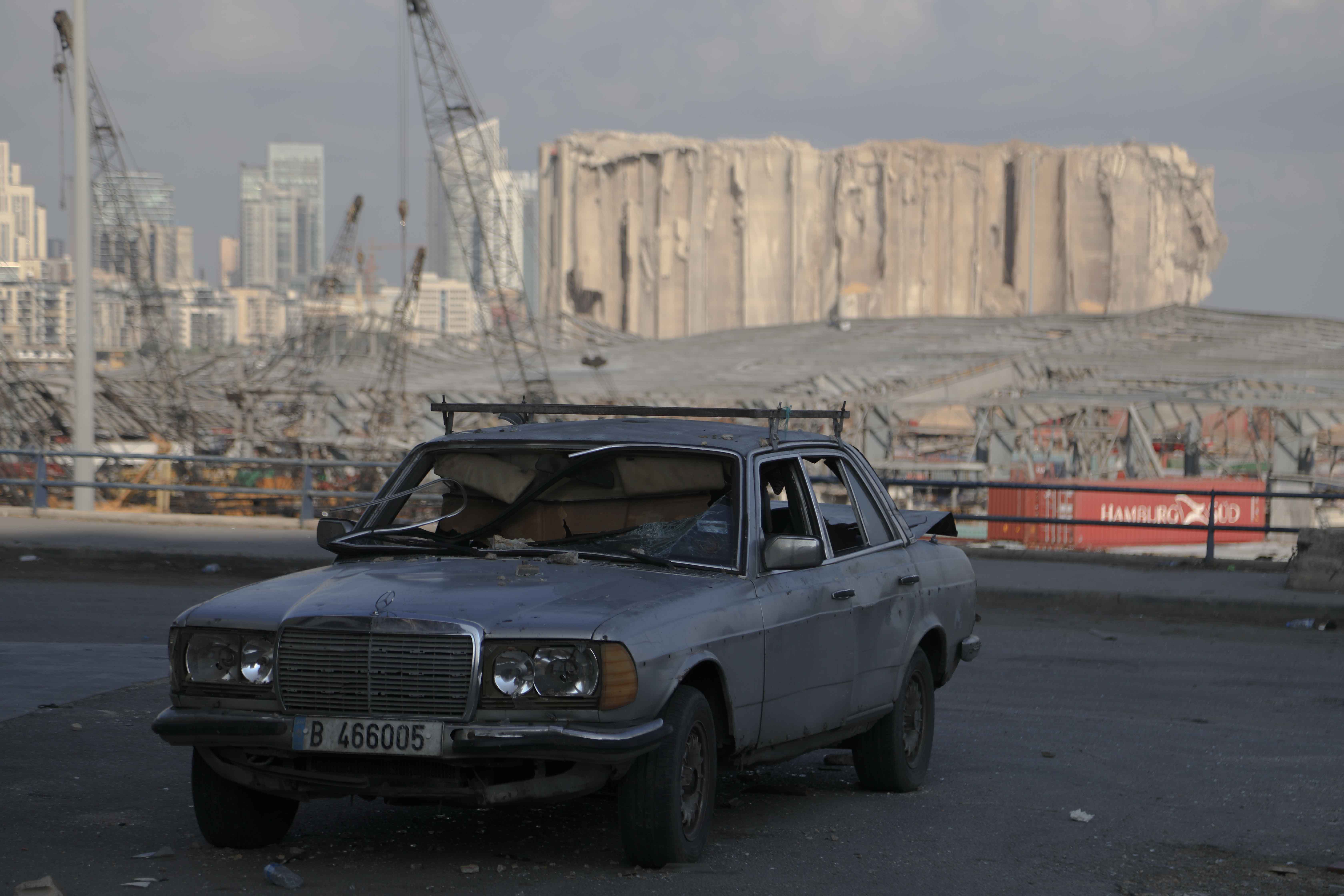A car in Lebanon sits damaged in front of the destruction of the port of Beirut post explosion