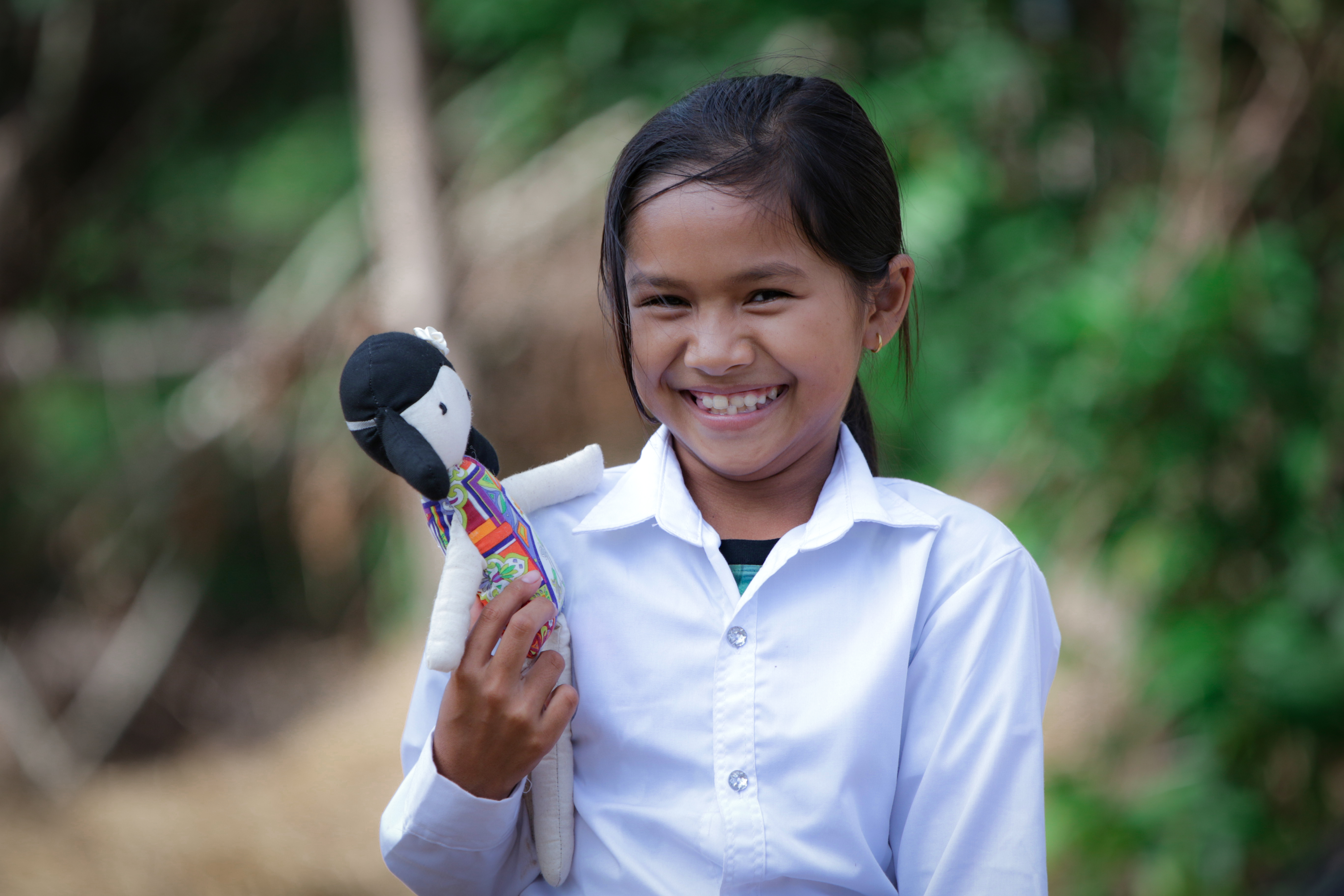 9 year old girl from Cambodia, smiles holding a doll and standing outside