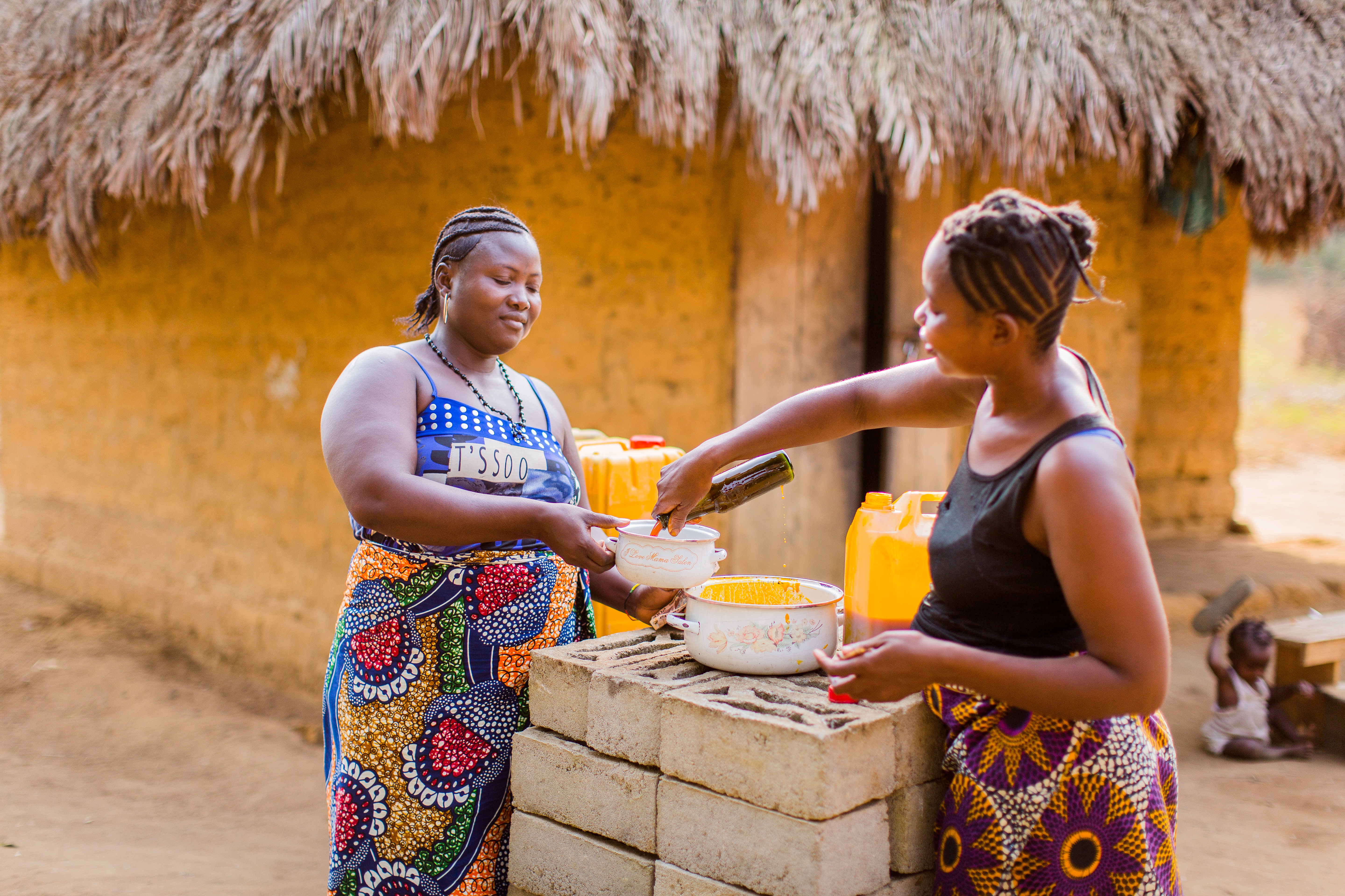 Two women in Sierra Leone smile as they cook together outside 