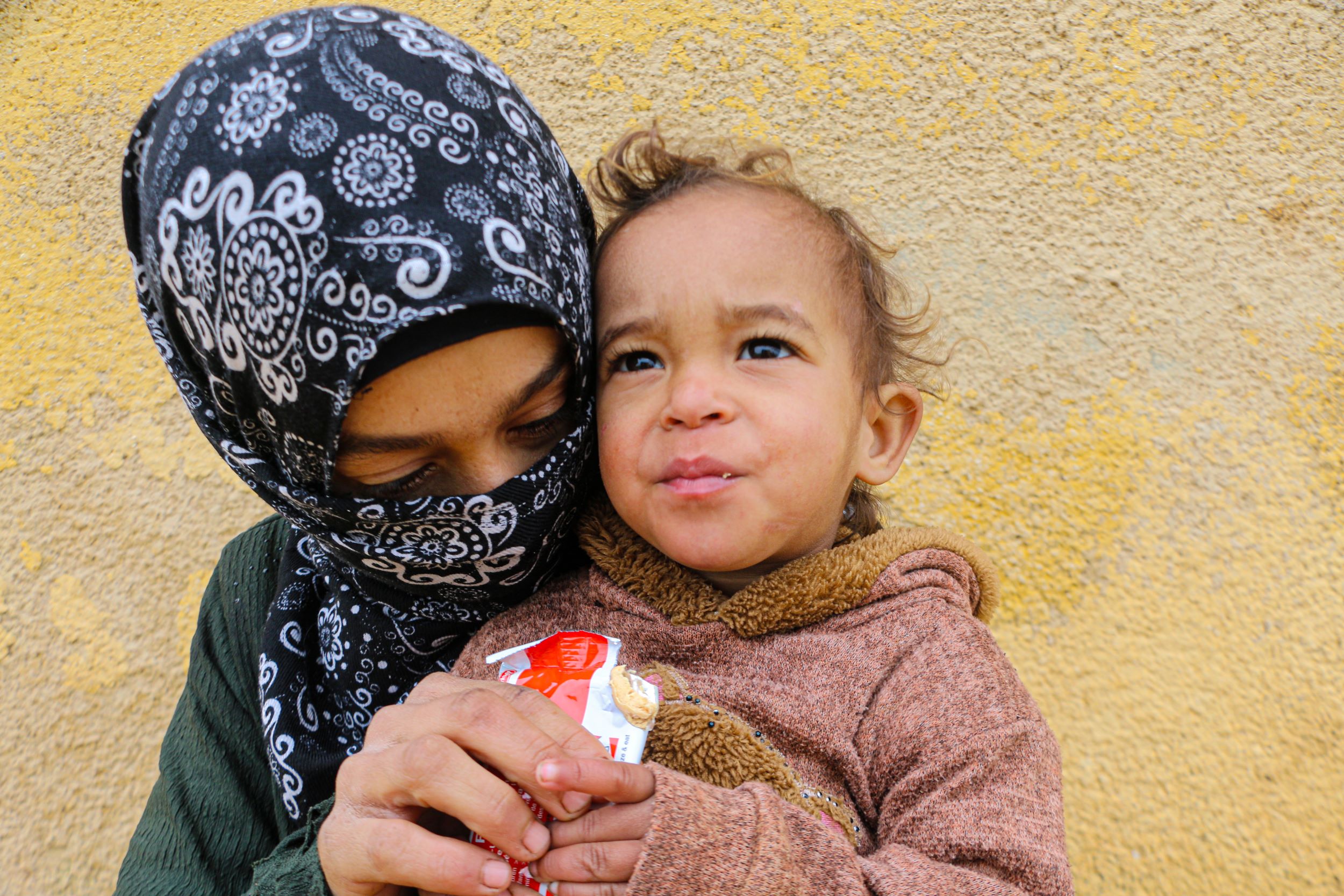 A baby held by her mother eating nutritional supplements to help her recover from malnutrition