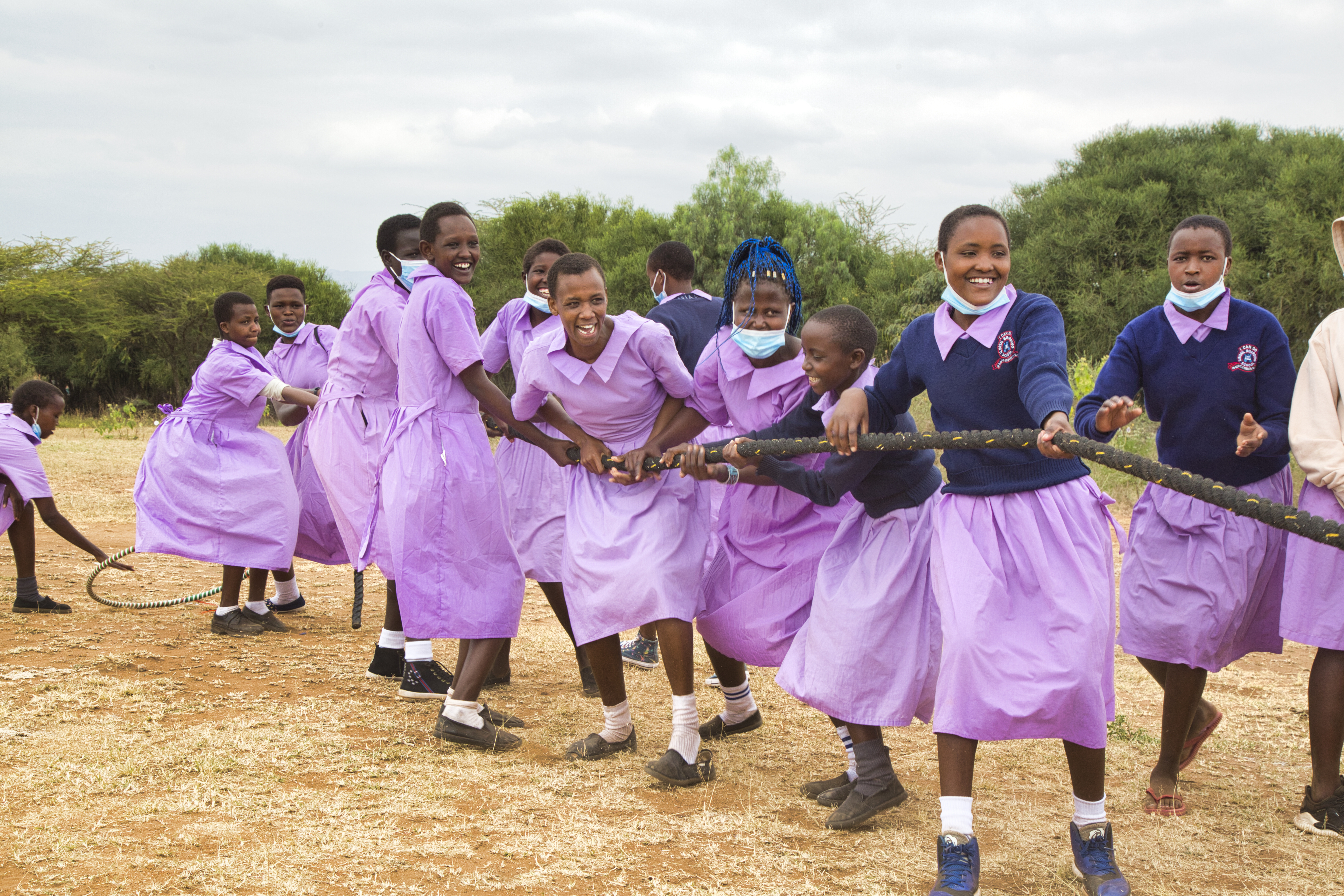 A group of girls, in purple school dresses, play tug of war