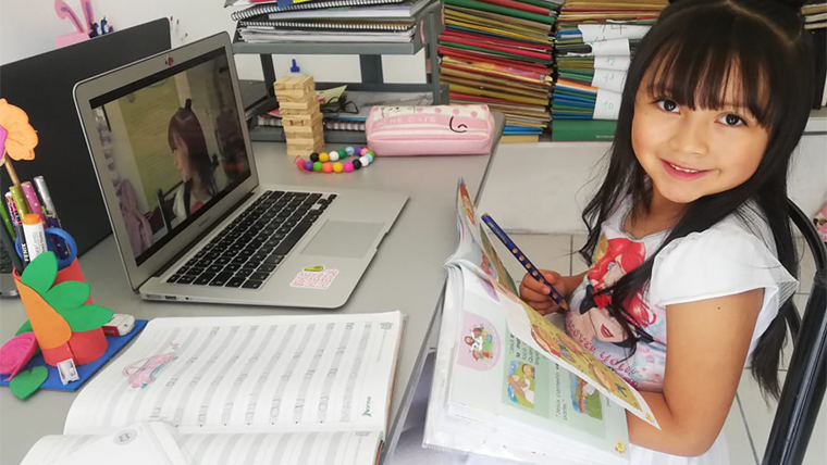 Girl sits at a desk on a video call, with her workbooks in front of her