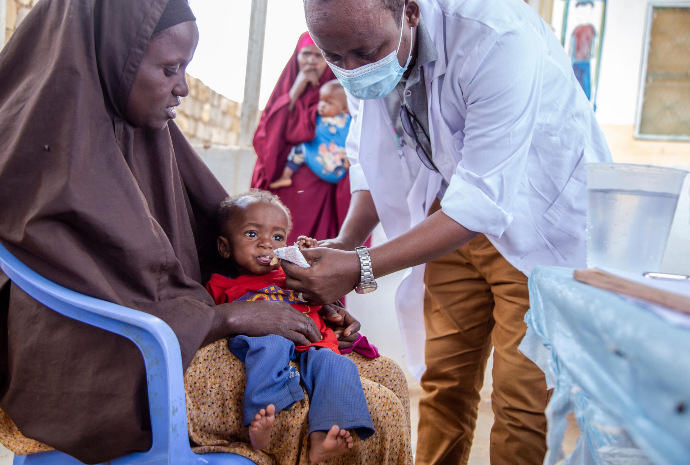 Somali woman wearing a hijab holding her young son while he is treated for malnutrition.