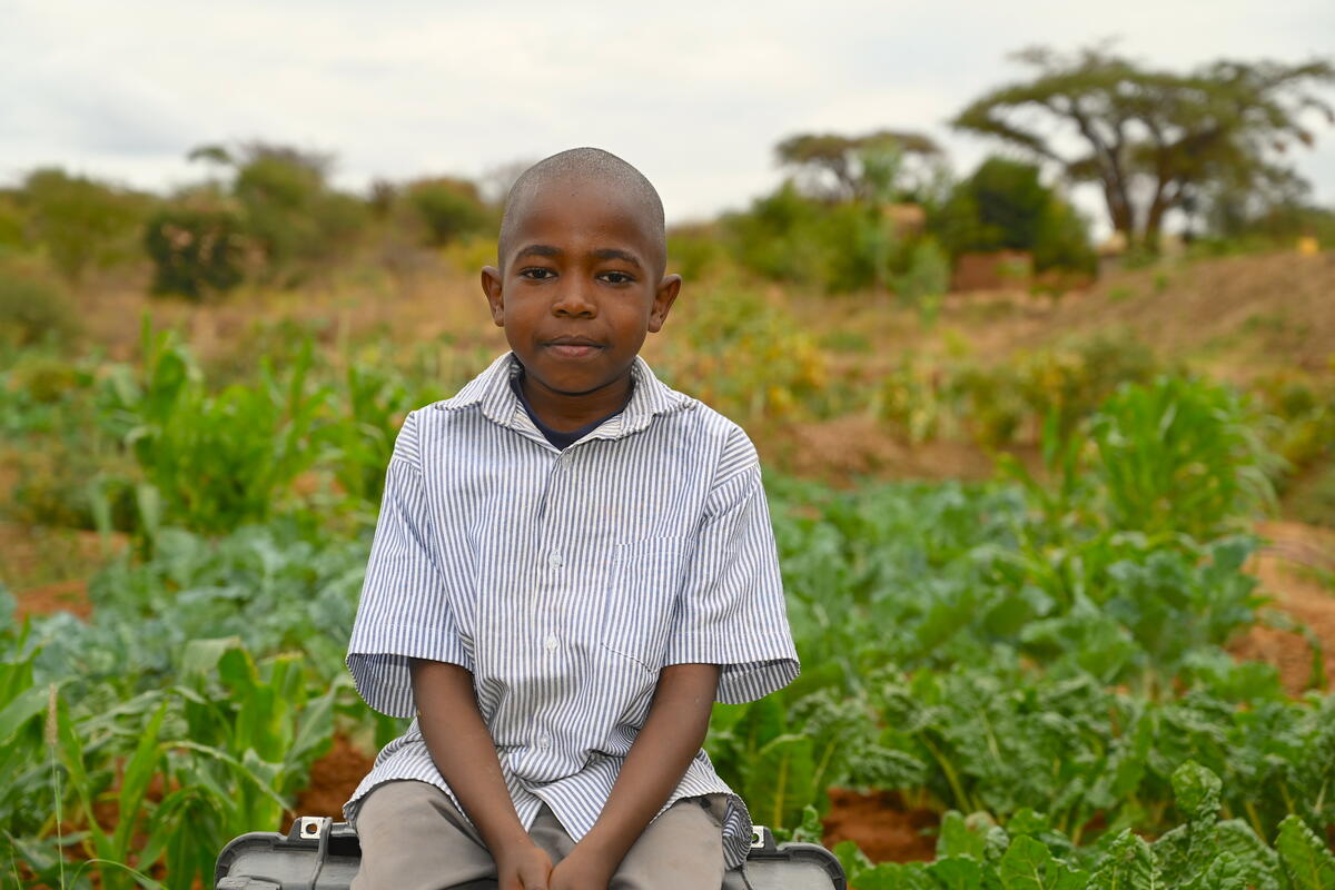 Kenyan boy sitting next to the family's crops