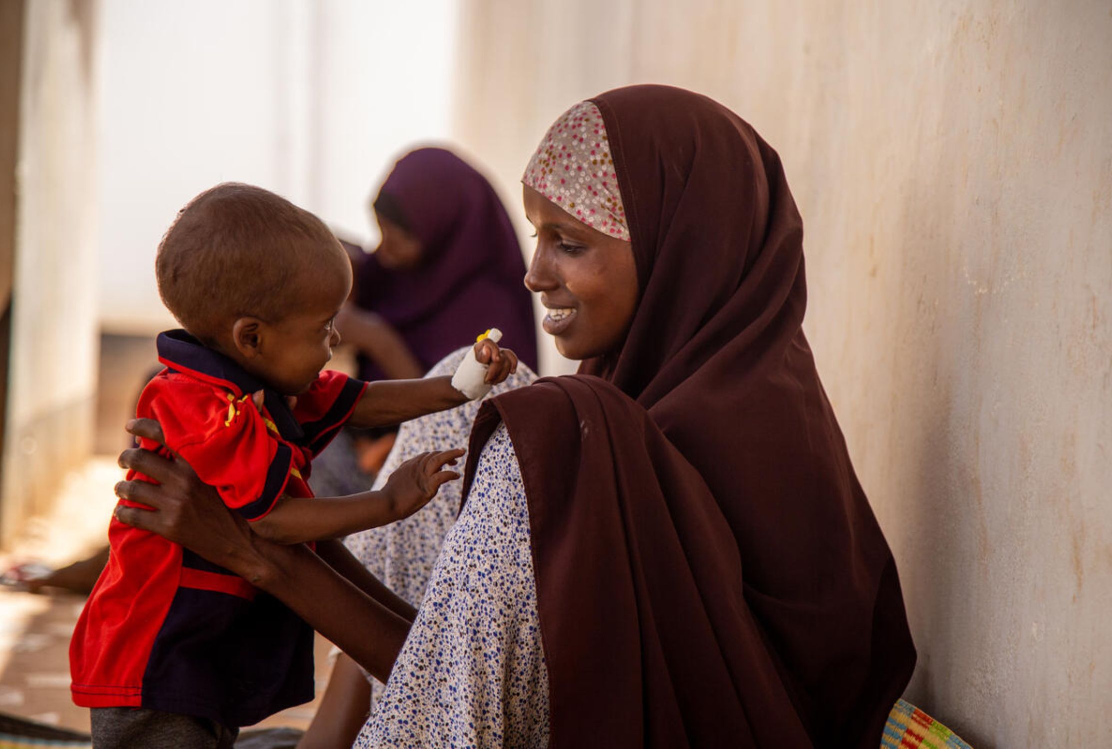 Somali mother wearing a hijab sits holding her child to stand up in front of her