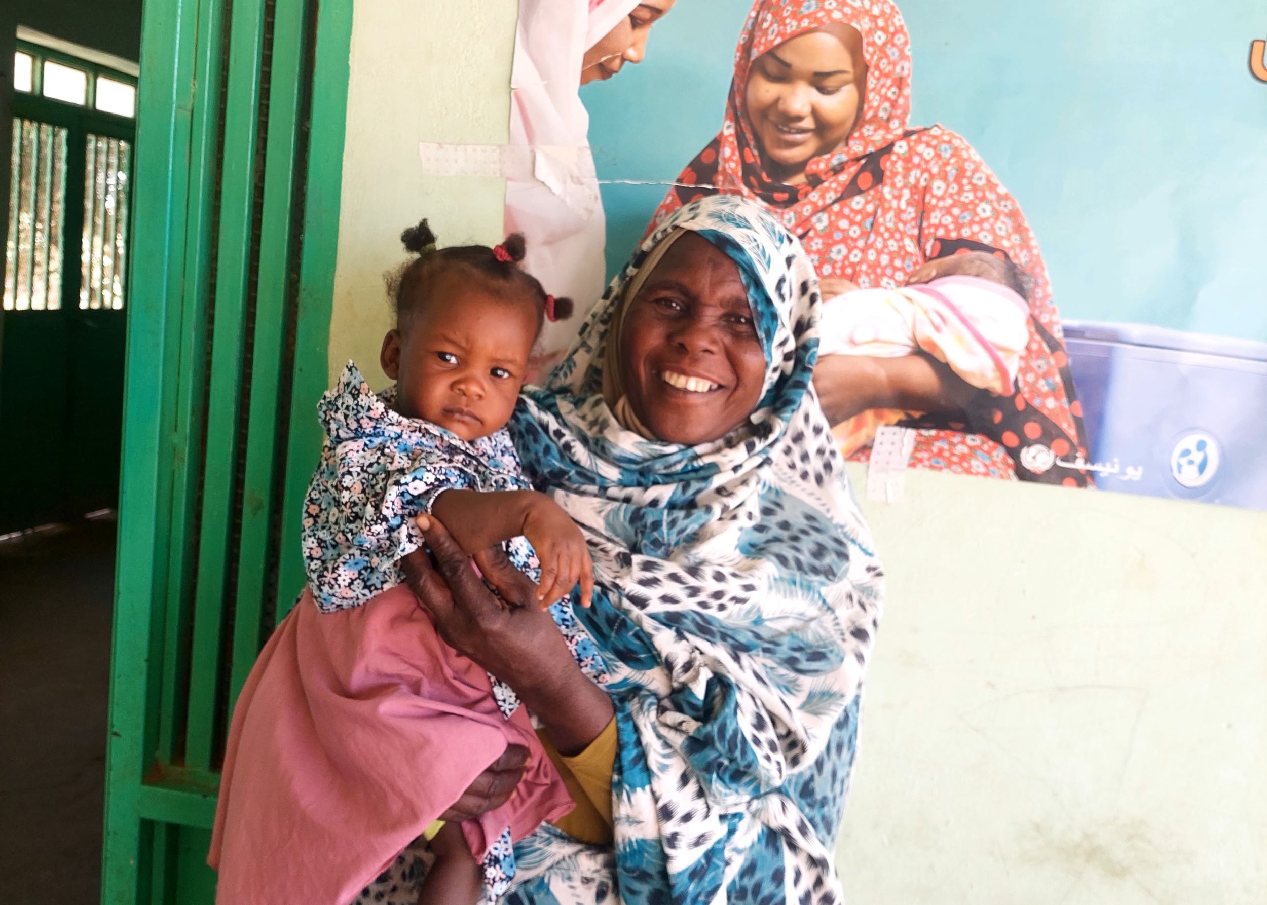 Smiling mother with blue and white headscarf holding baby girl 