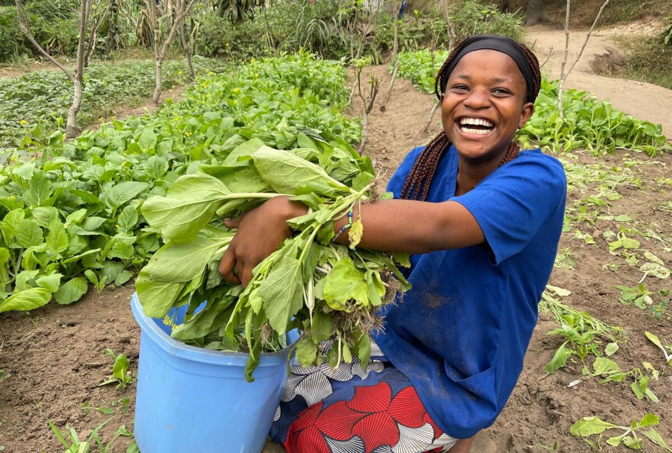 Teenage girl from the DRC smiling as she holds up the vegetable produce she has grown