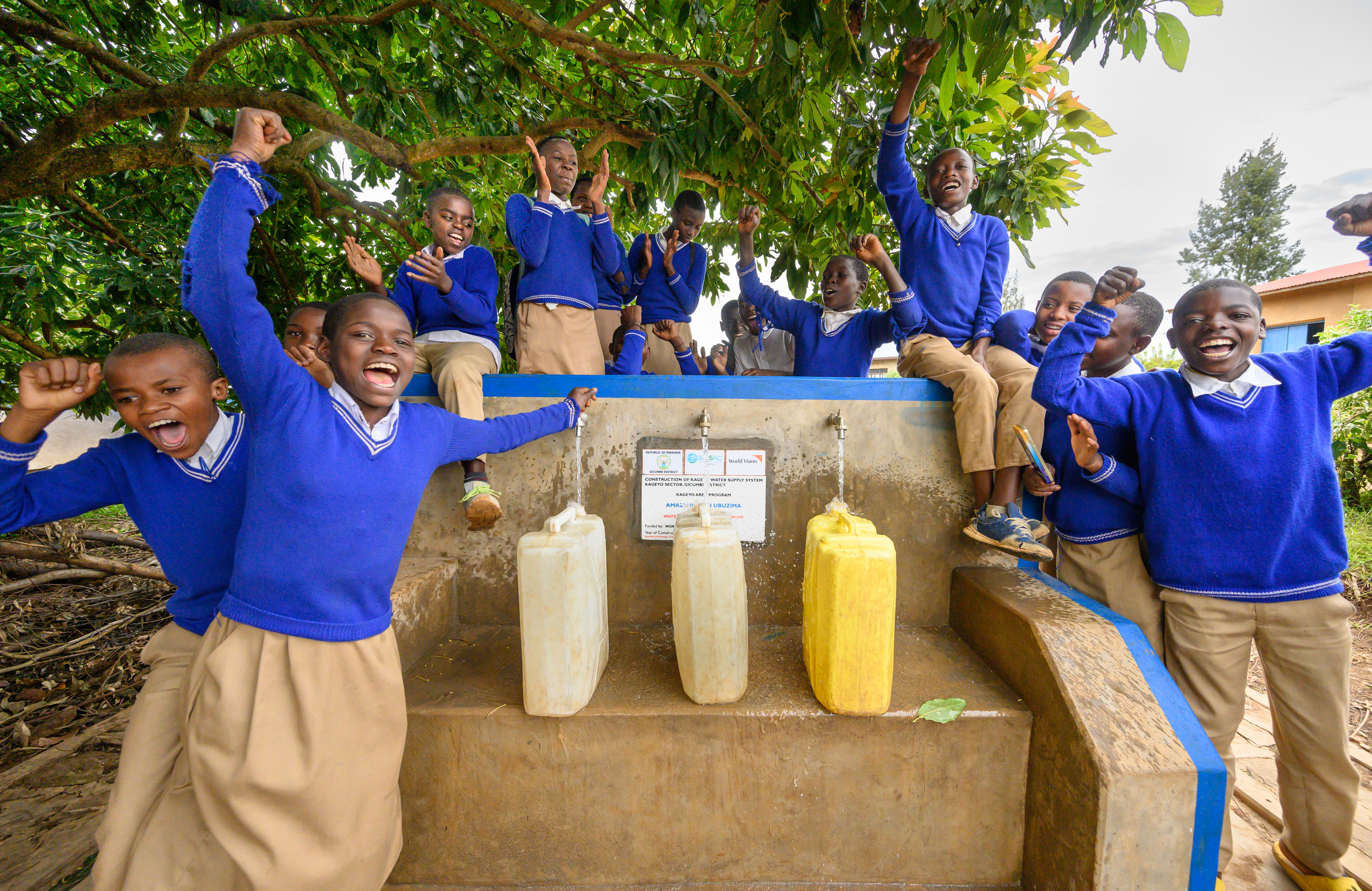 A group of school children in their uniforms celebrate around the taps as they fill jerricans with safe drinking water