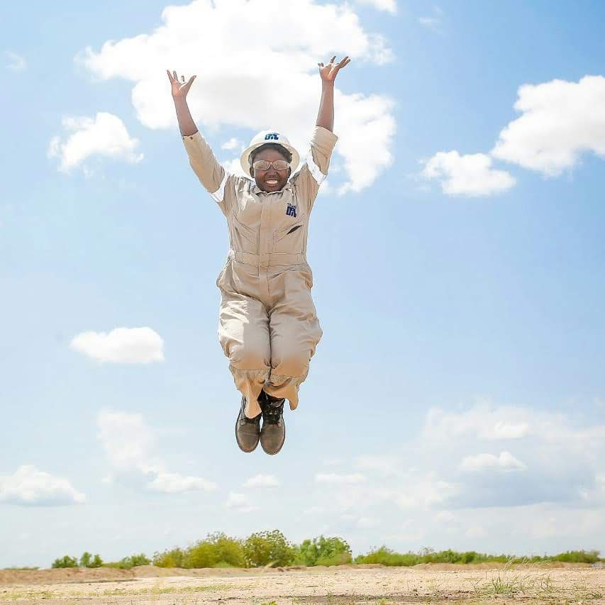 Pauline, wearing hard hat and overalls, jumps for joy during her internship
