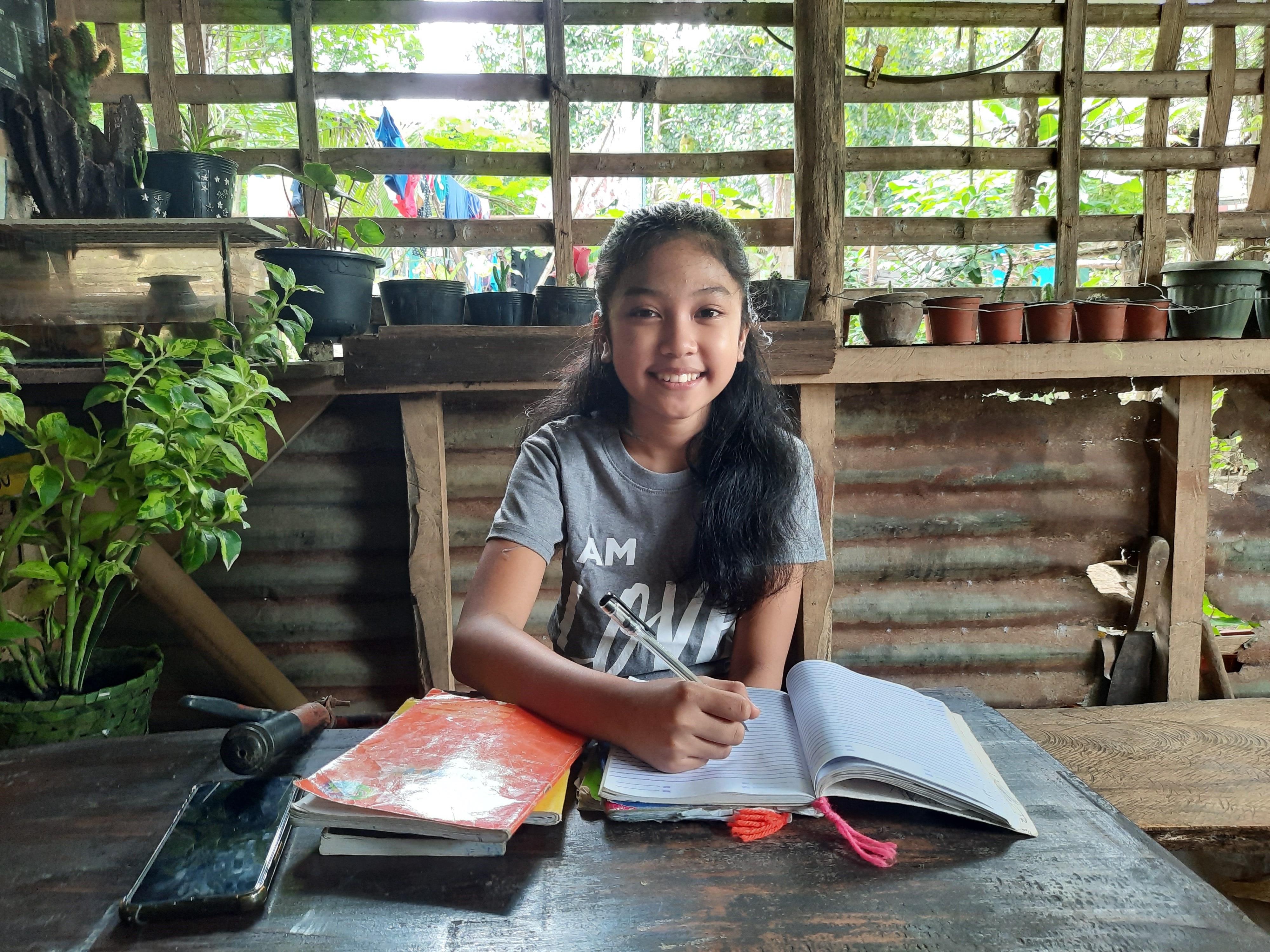 Girl in the Philippines sits at a desk with her workbook, working from home because of COVID-19