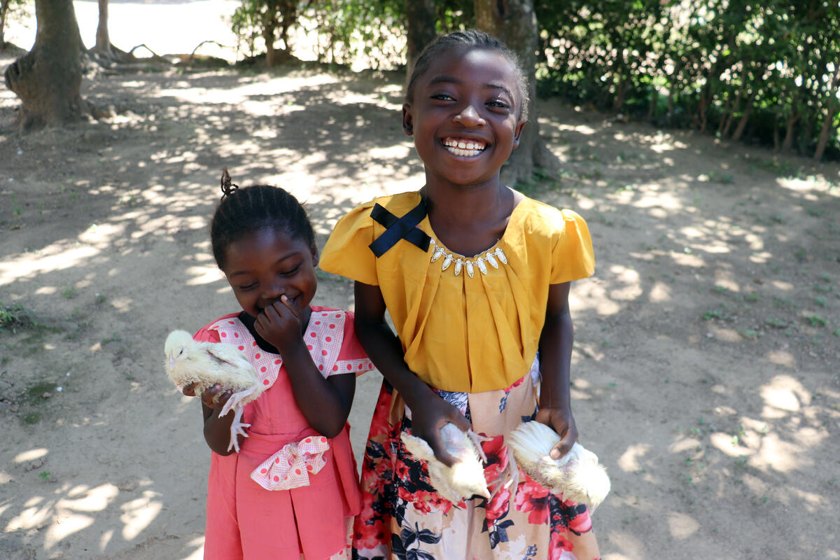 Two young girls from the DRC holding two baby chicks each and smiling