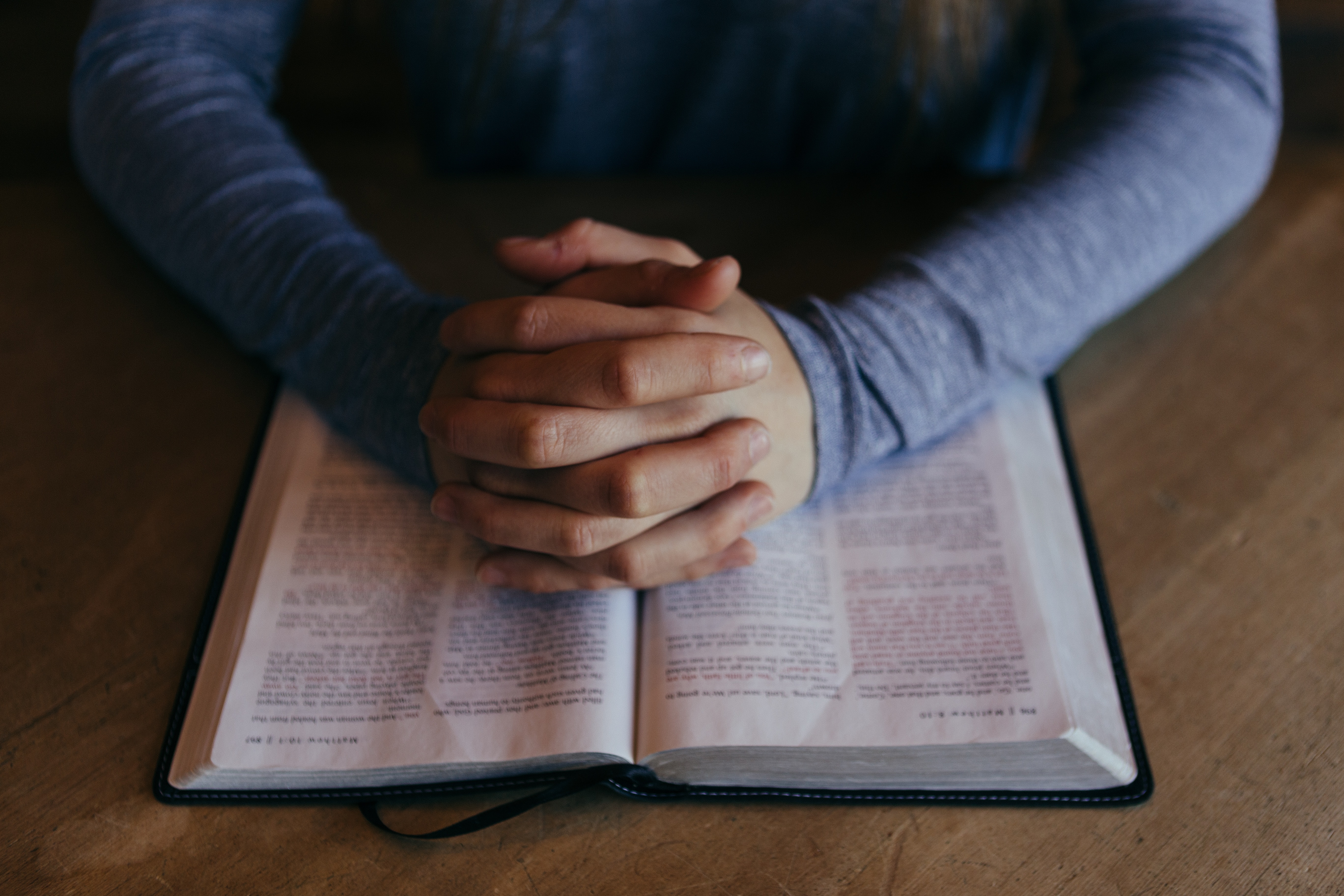 Hands rested on an open Bible in a prayer position