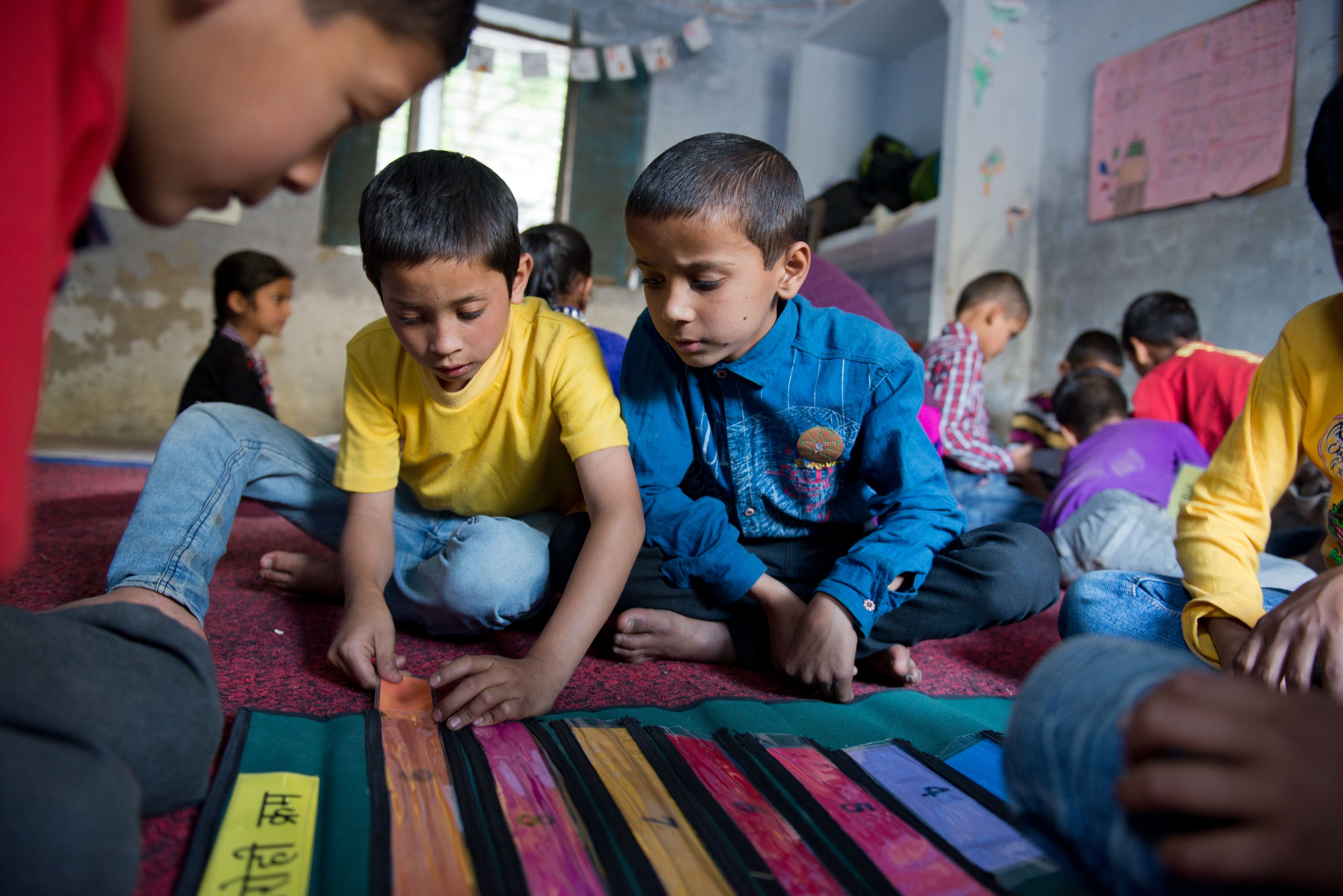 Two boys sit on the floor in a centre in India and play with educational tools