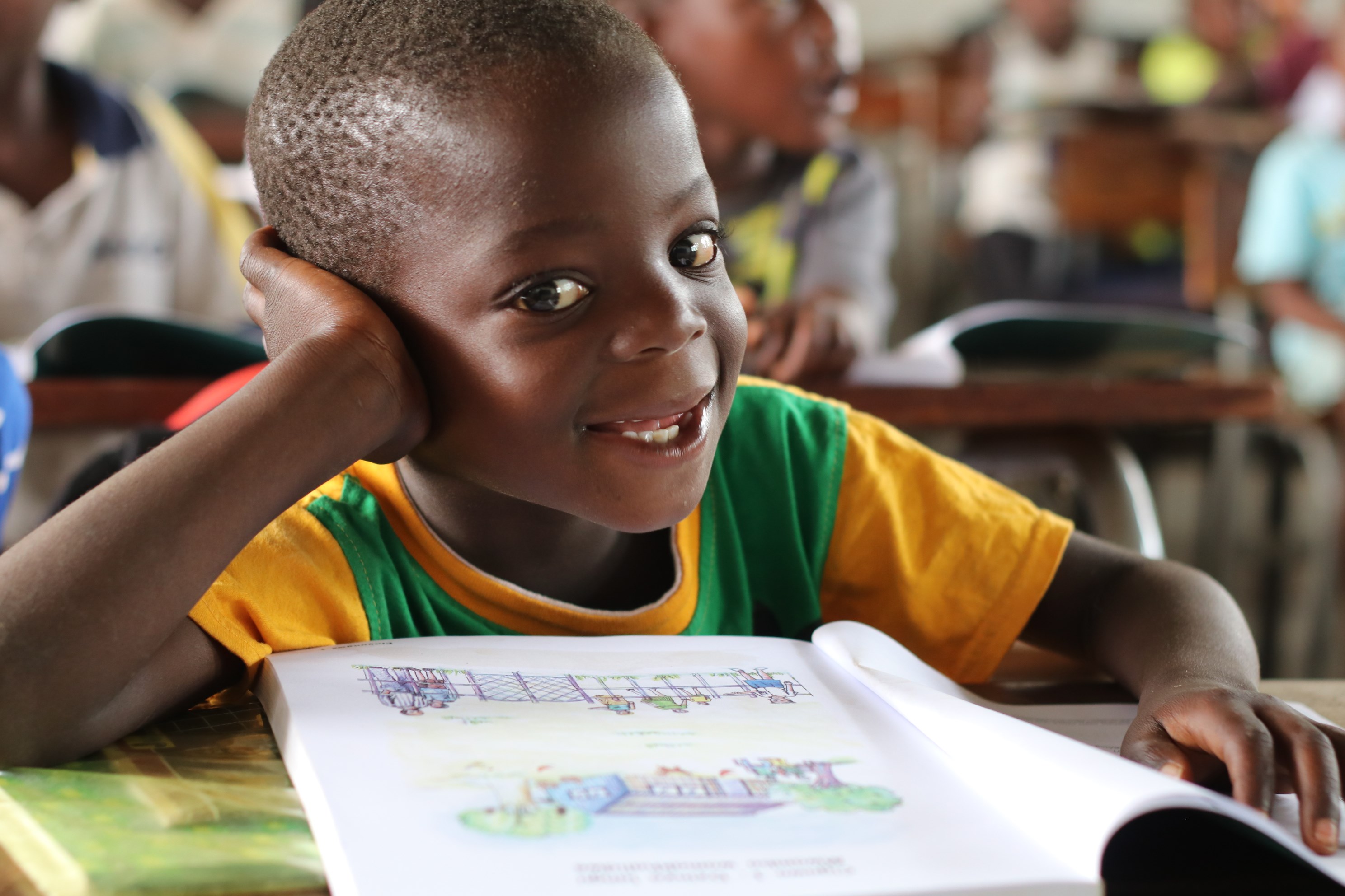 Child from Mozambique sits at a desk in a classroom, book open in front of him