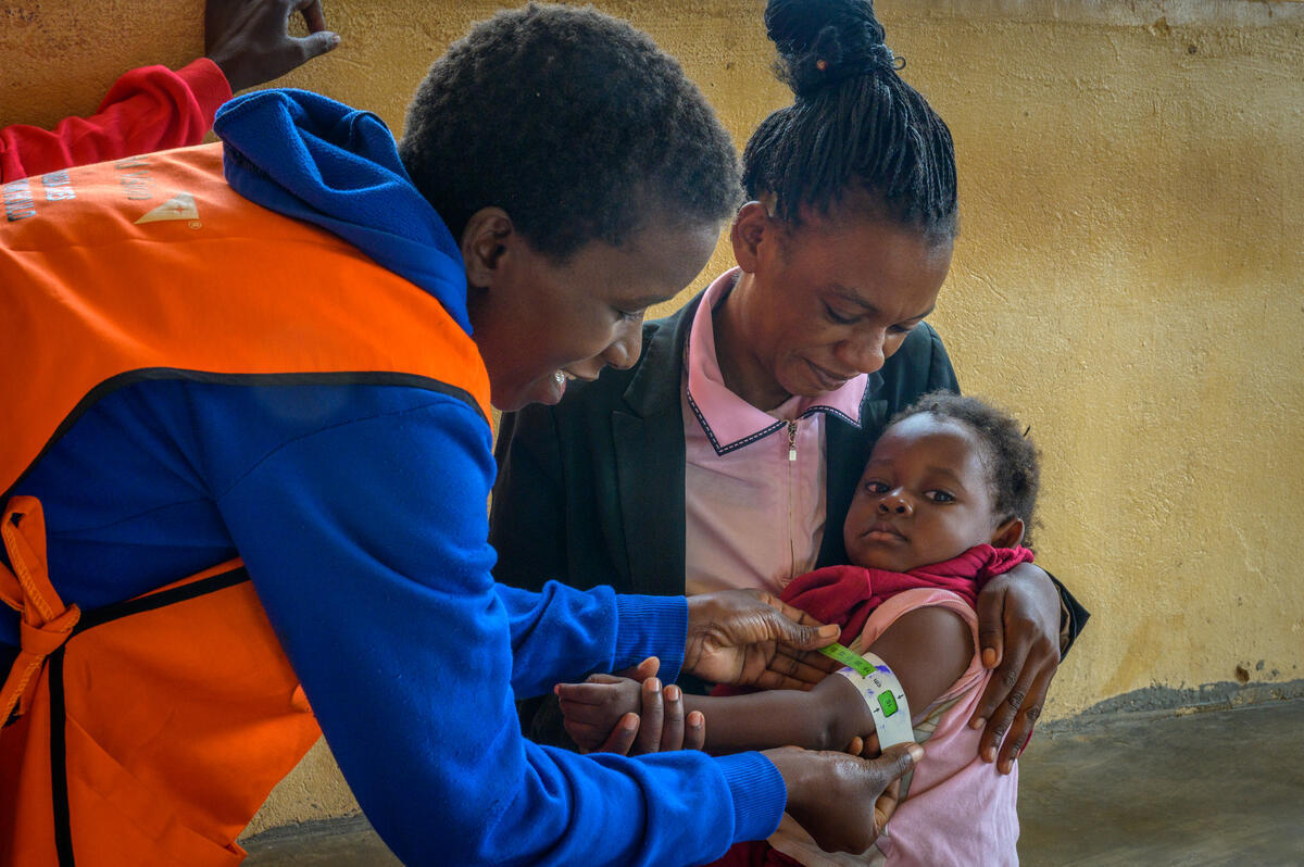 A child in Zambia, held by their mother, while receiving medical support from health worker