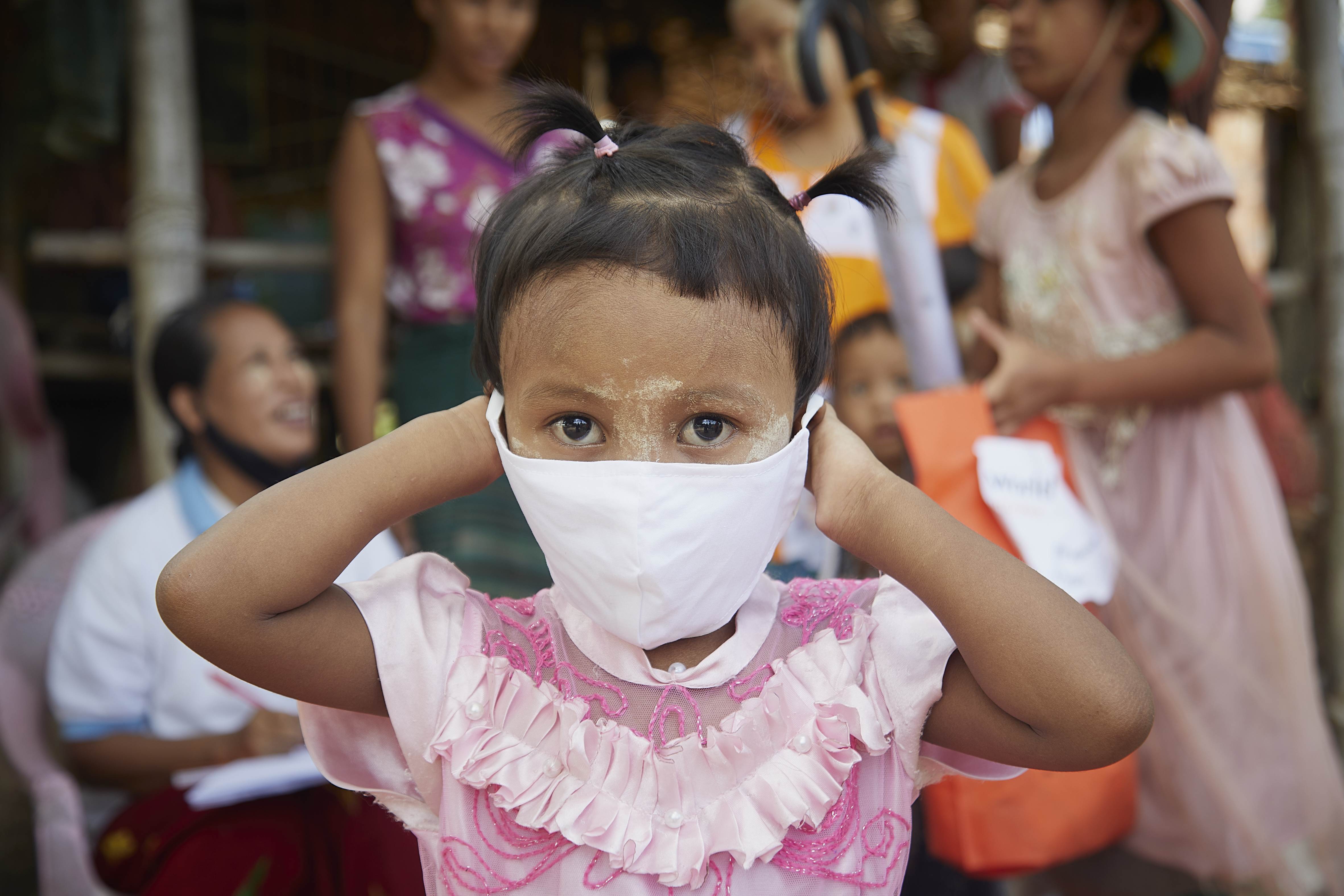 Girl from Myanmar puts a mask onto her face against the backdrop of other people