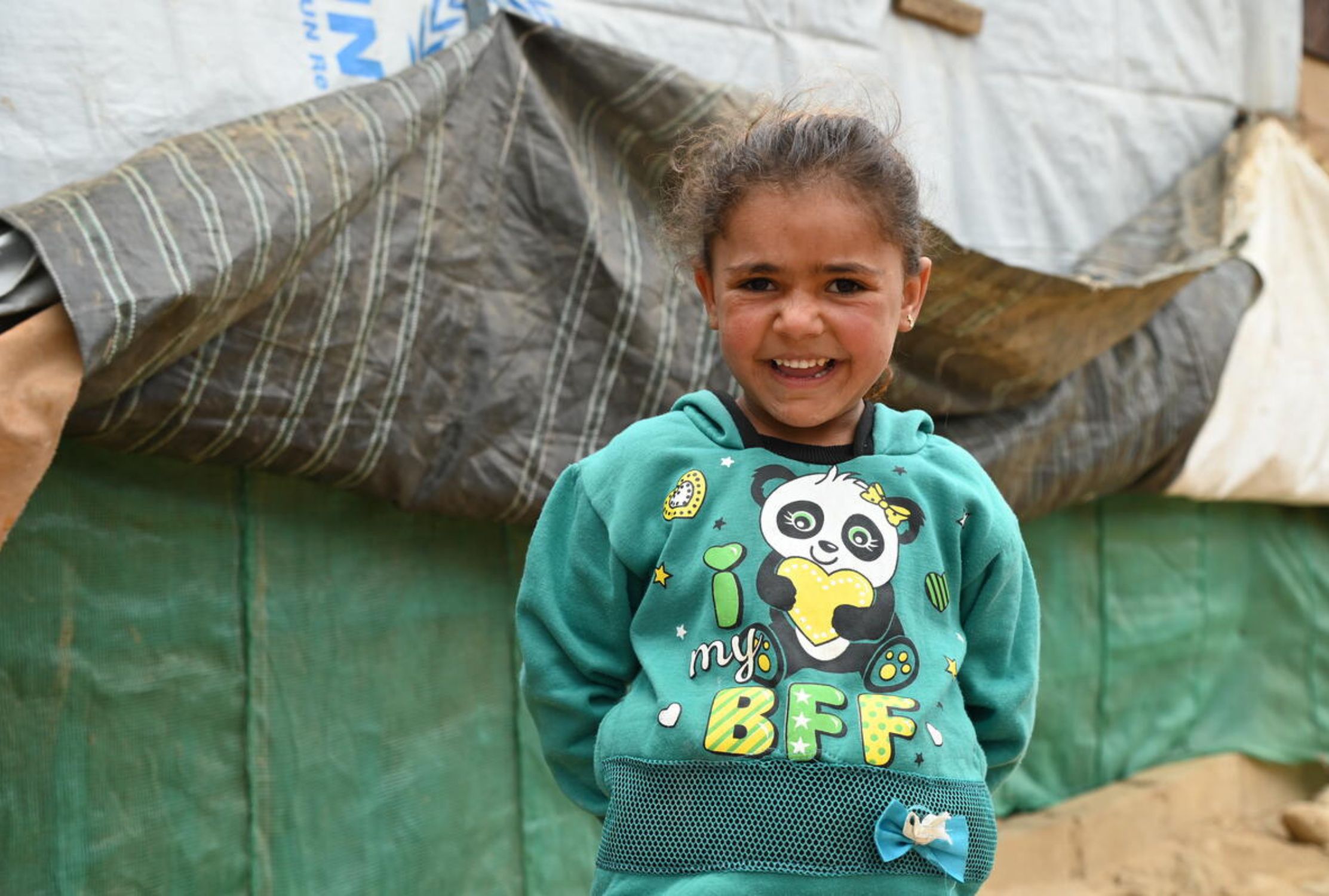 Girl in Lebanon looking at the camera while standing in front of a temporary shelter