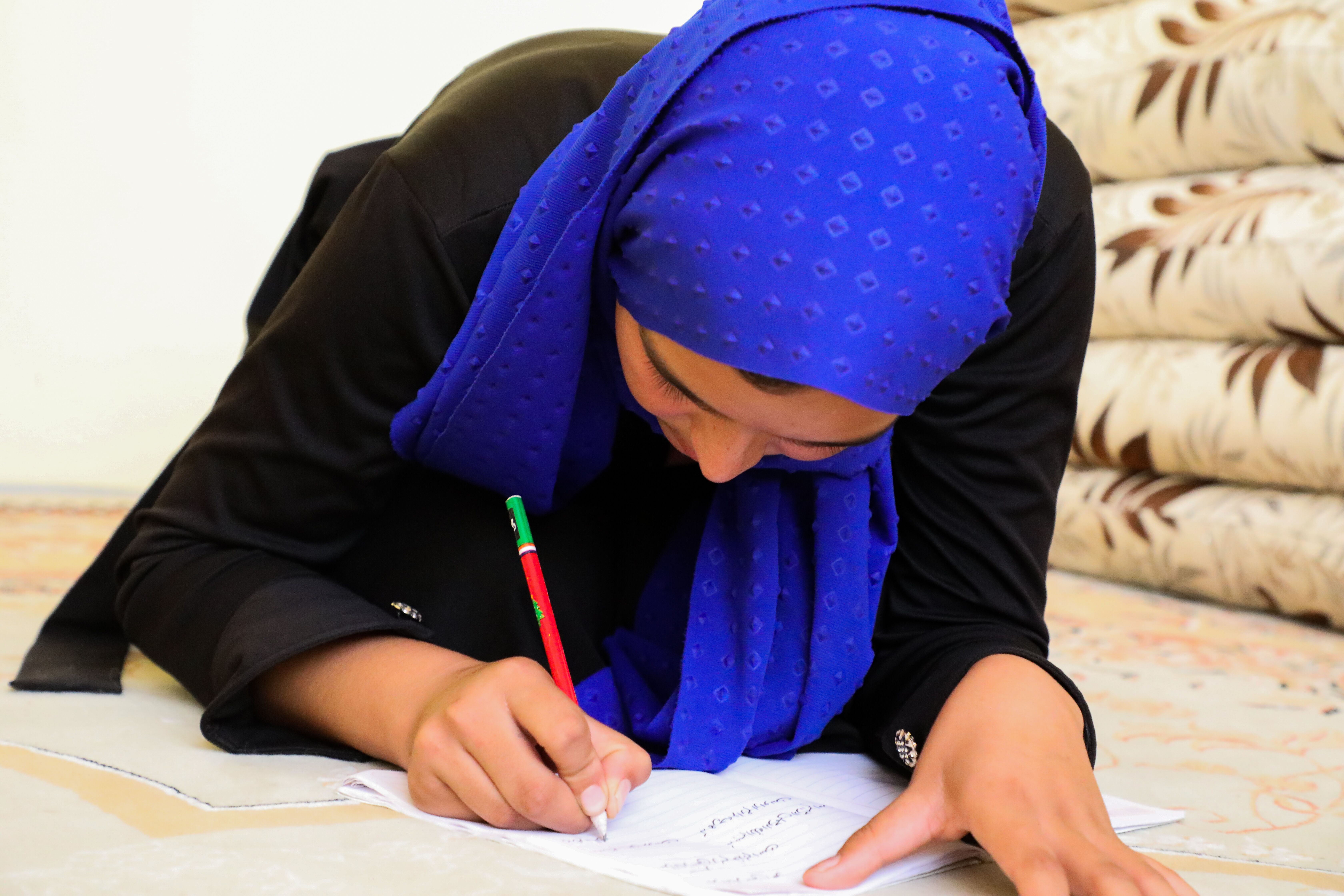 Girl in Afghanistan bends over her paper, writing on it on the floor