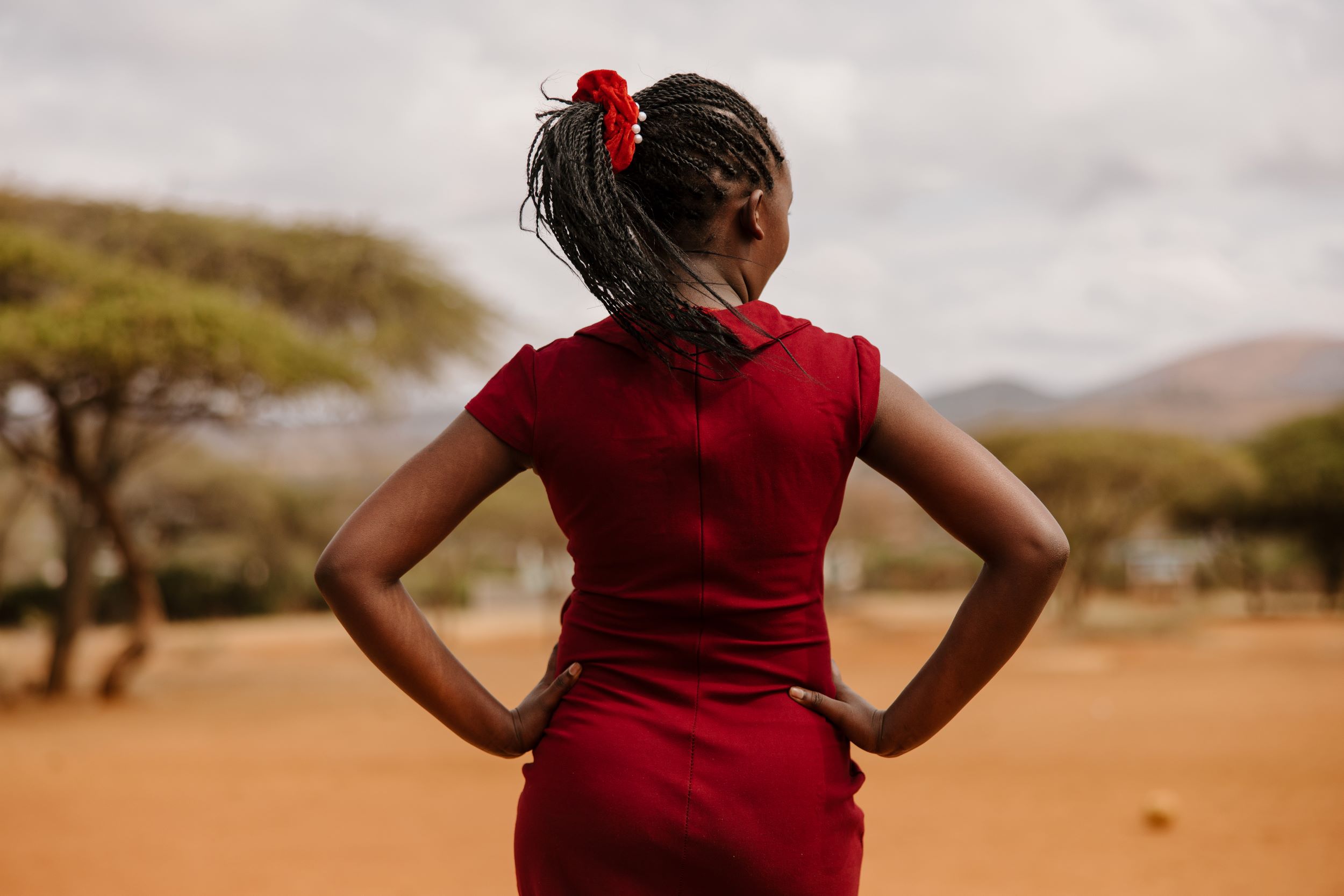 Kenyan girl in red dress stands hopeful with hands on hips. 