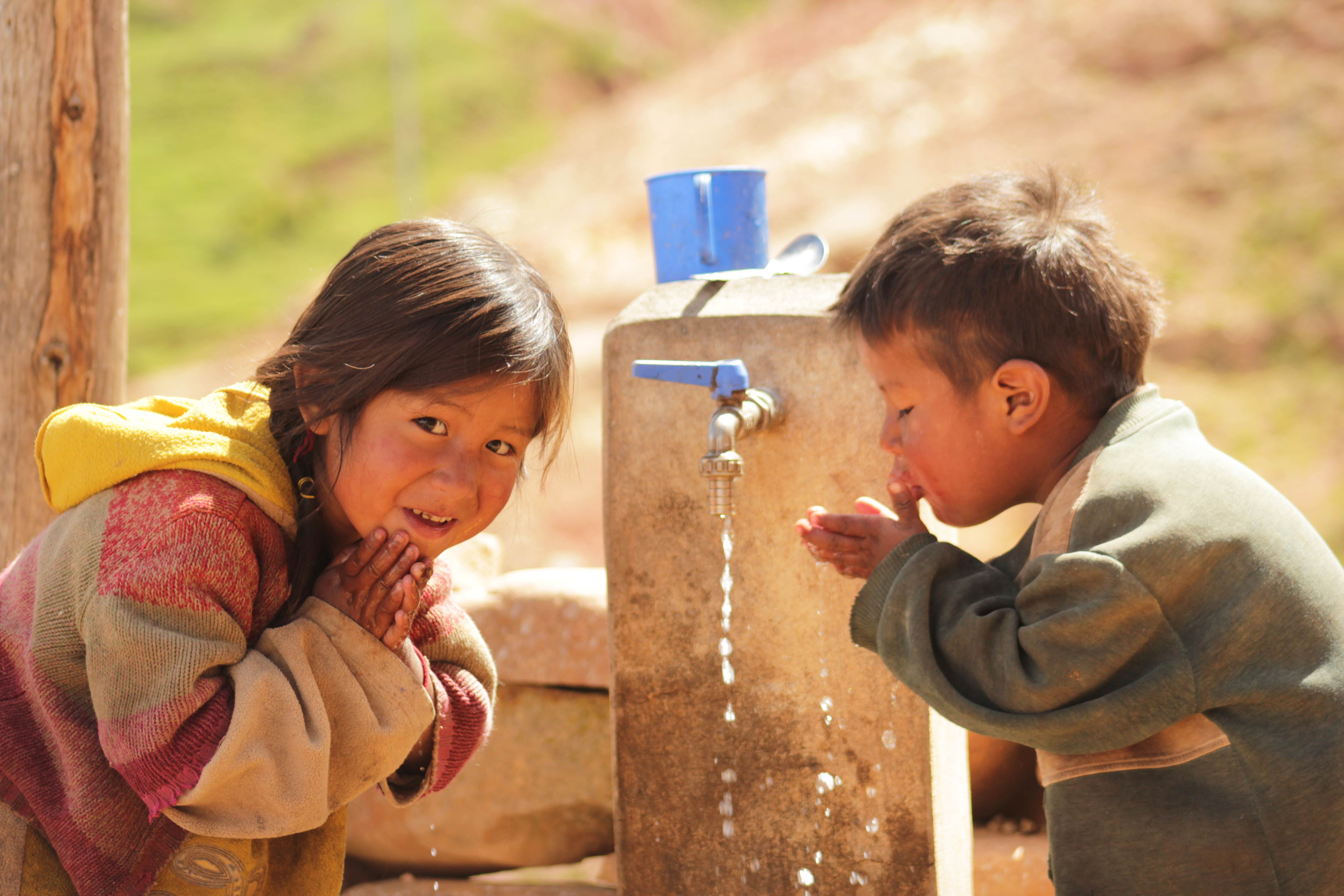 A young girl and boy in Bolivia, get clean water from a new tap near their home